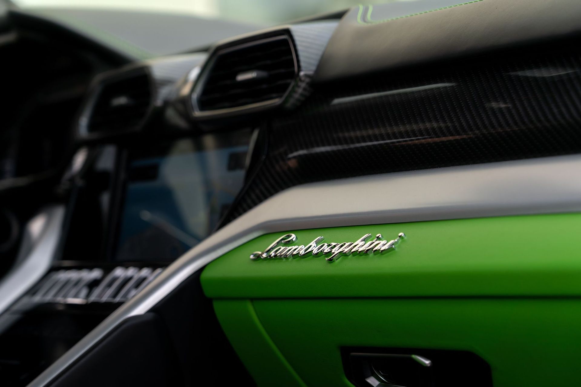 Interior of a Lamborghini with green accents, carbon fiber trim, and the Lamborghini logo.