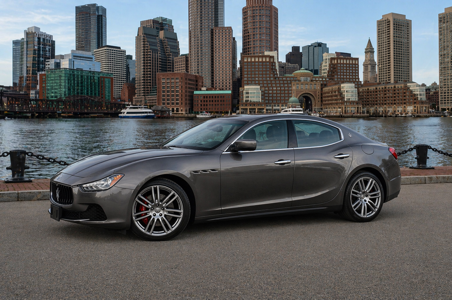 Gray sports sedan parked by a waterfront with a city skyline in the background