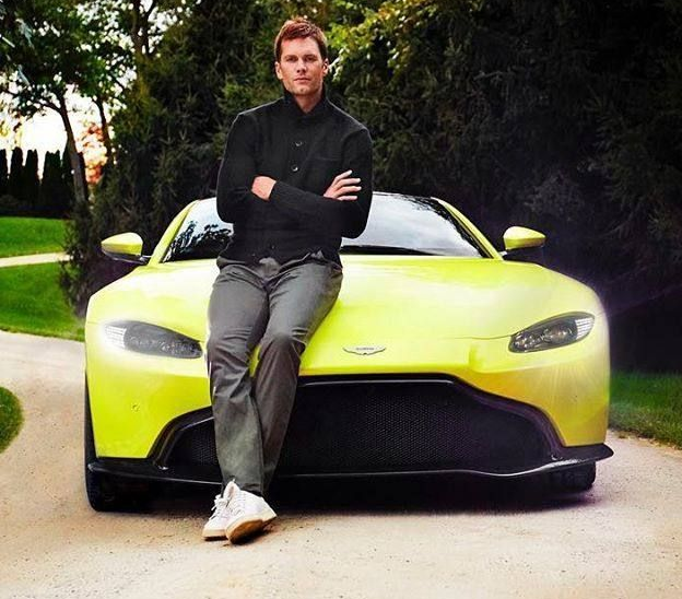 Tom Brady leaning on a bright yellow Aston Martin.