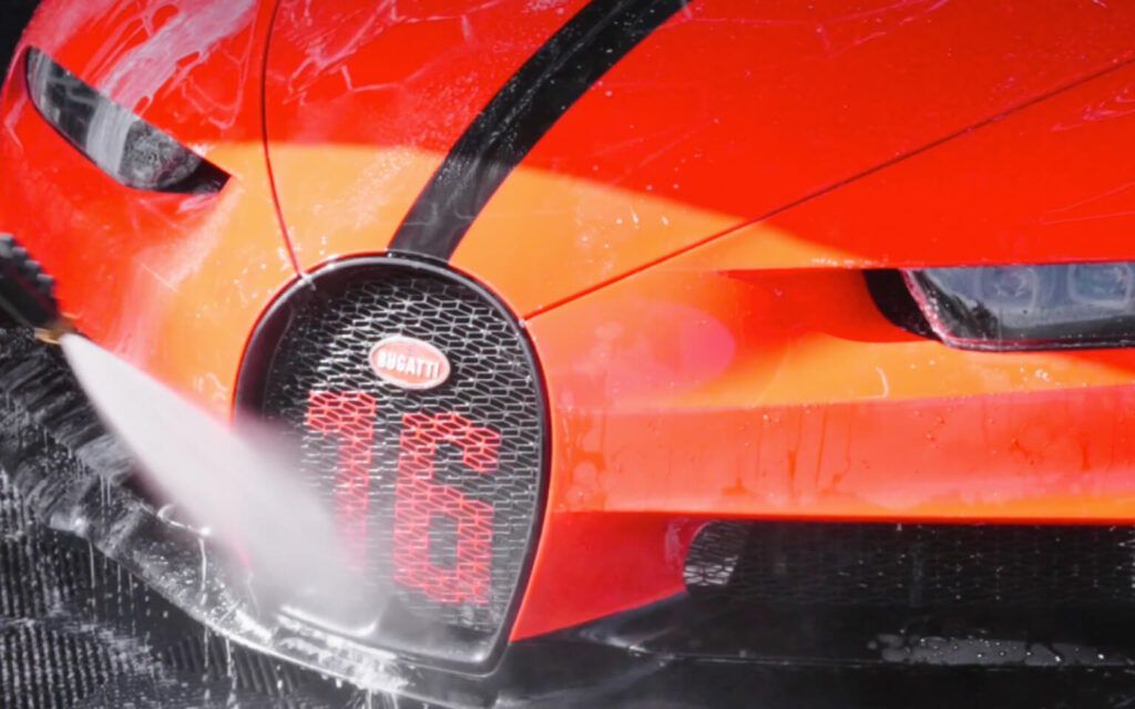 Close-up of a red Bugatti being washed with water spray. Grille has the Bugatti logo and large 88.