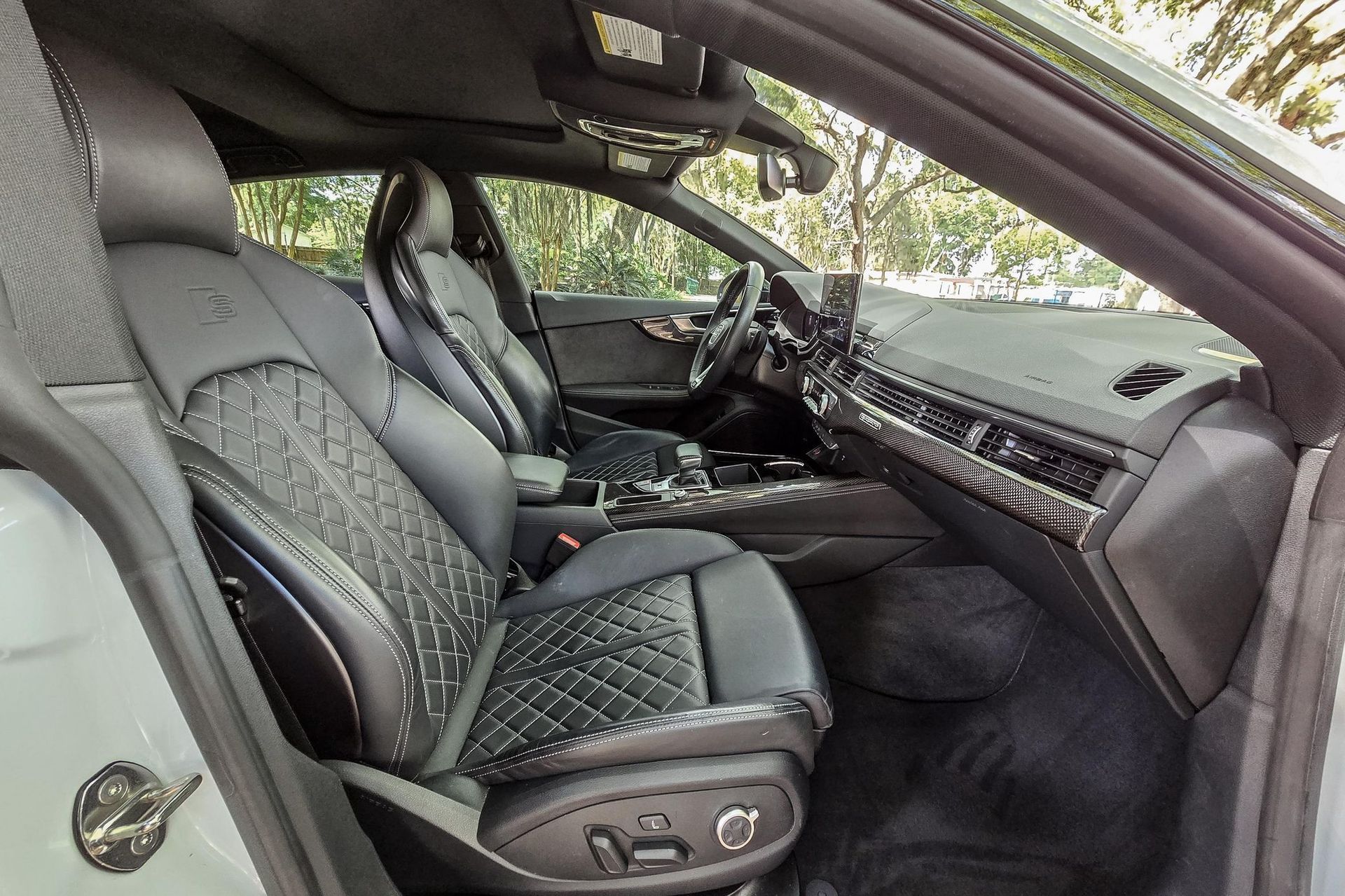 Interior view of a black leather car with quilted seats, dashboard, and steering wheel; sunlight streams in.