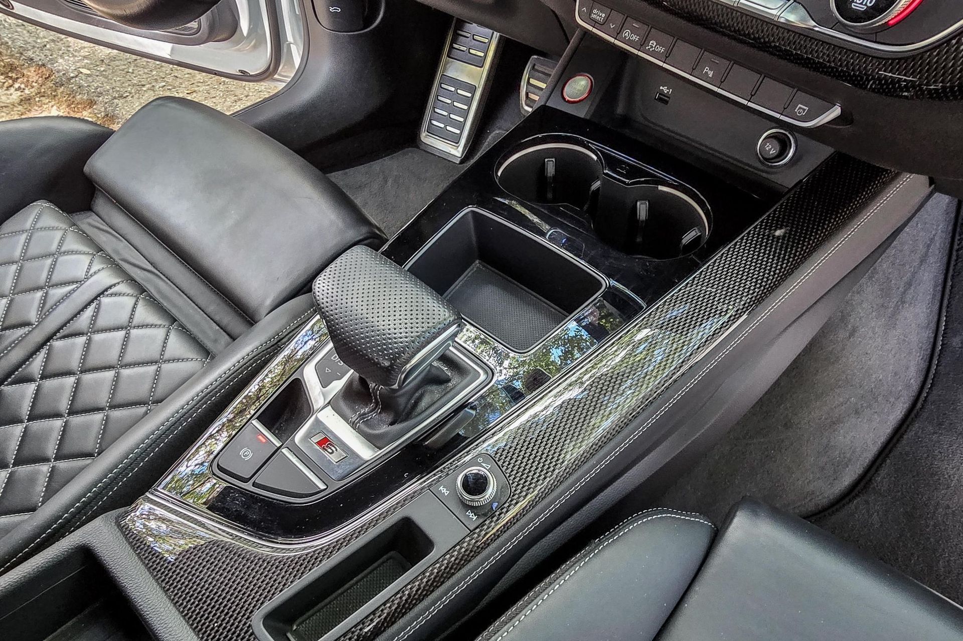 Interior of a car's center console with carbon fiber trim, gear shift, cup holders, and black leather seats.