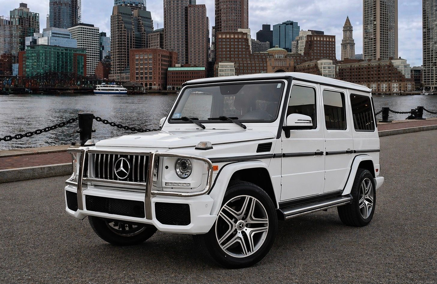 White Mercedes-Benz G-Wagon SUV parked on a rooftop with a city skyline in the background.