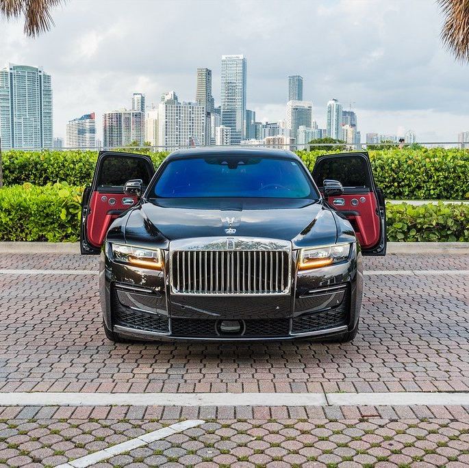 Black Rolls Royce with red doors open, parked on brick, city skyline in background.