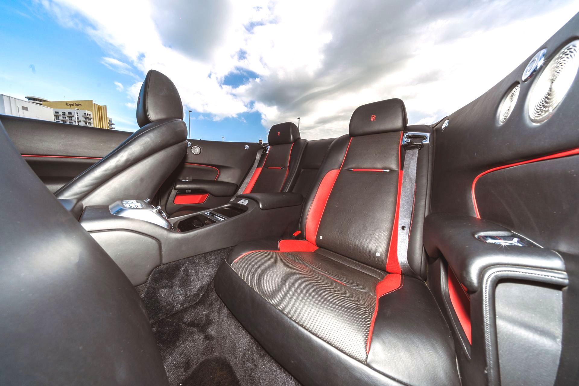 Interior of a black and red sports car with leather seats under a cloudy sky.