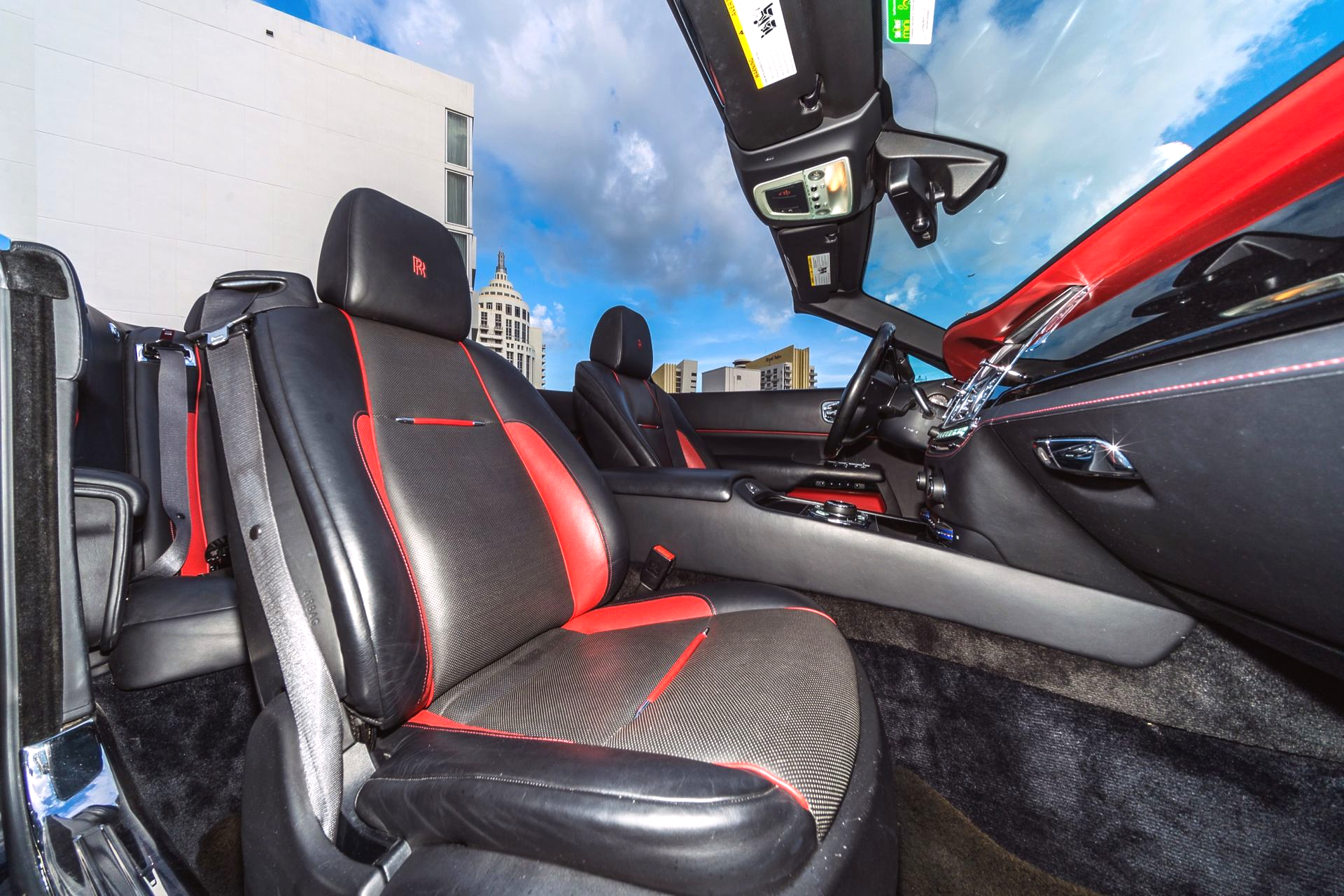 Interior of a convertible car with black and red leather seats. The top is down, showing a blue sky.