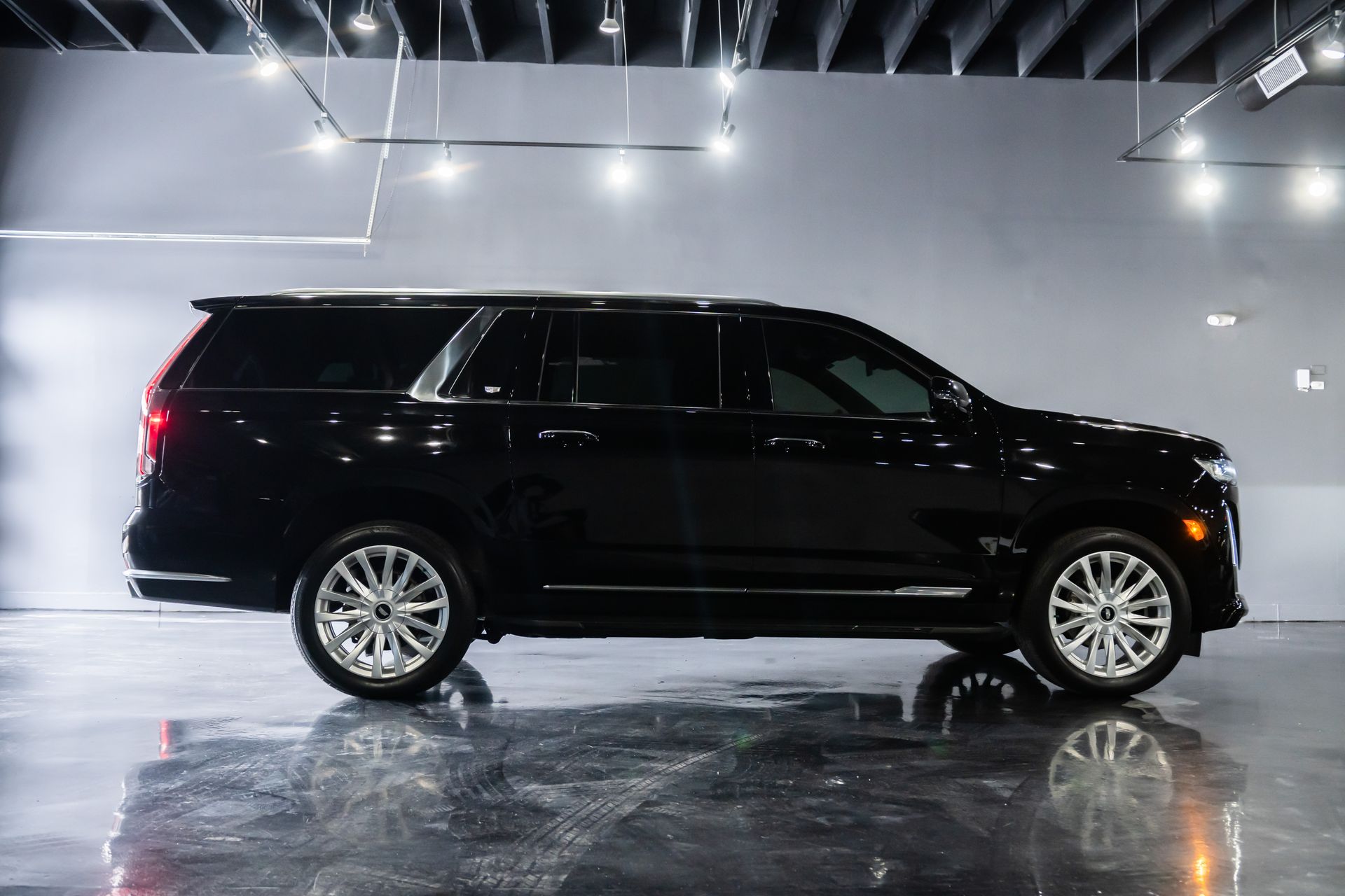 Black Cadillac SUV in a showroom, silver wheels, glossy black paint, bright lighting.