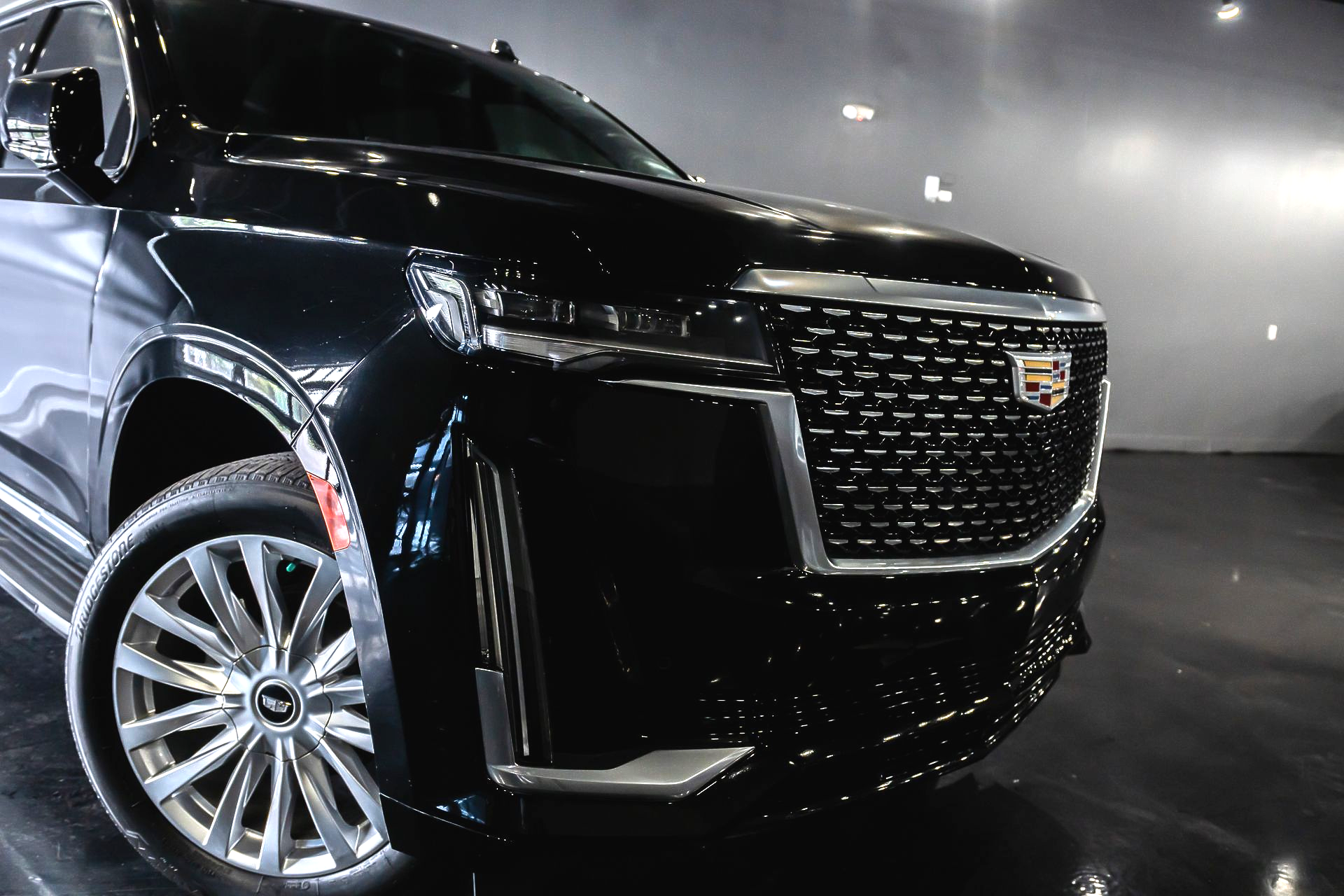Black Cadillac SUV, front view, chrome grill, shiny, indoors.
