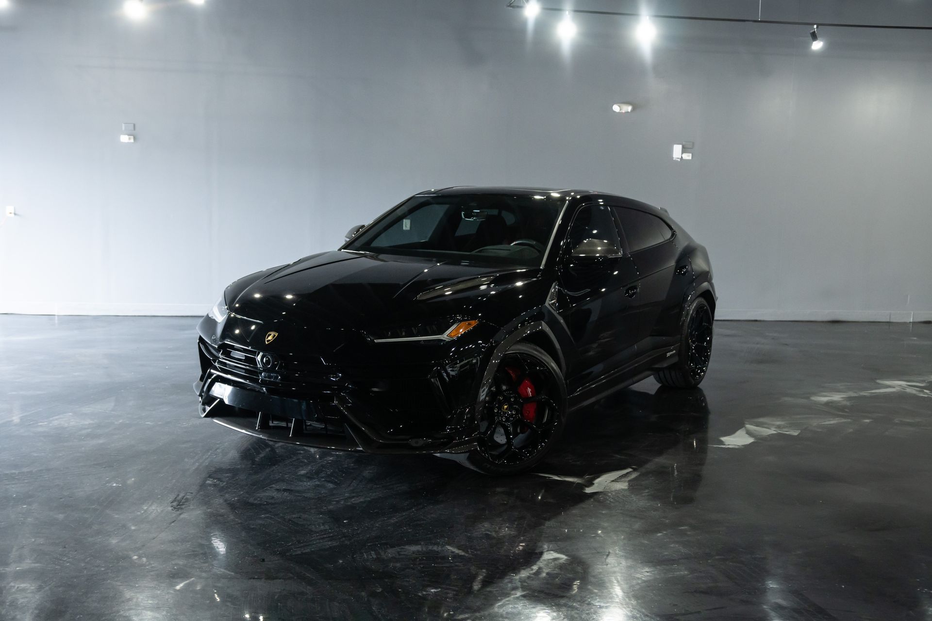 Black Lamborghini Urus SUV parked in a studio with bright overhead lights reflecting on the glossy floor.