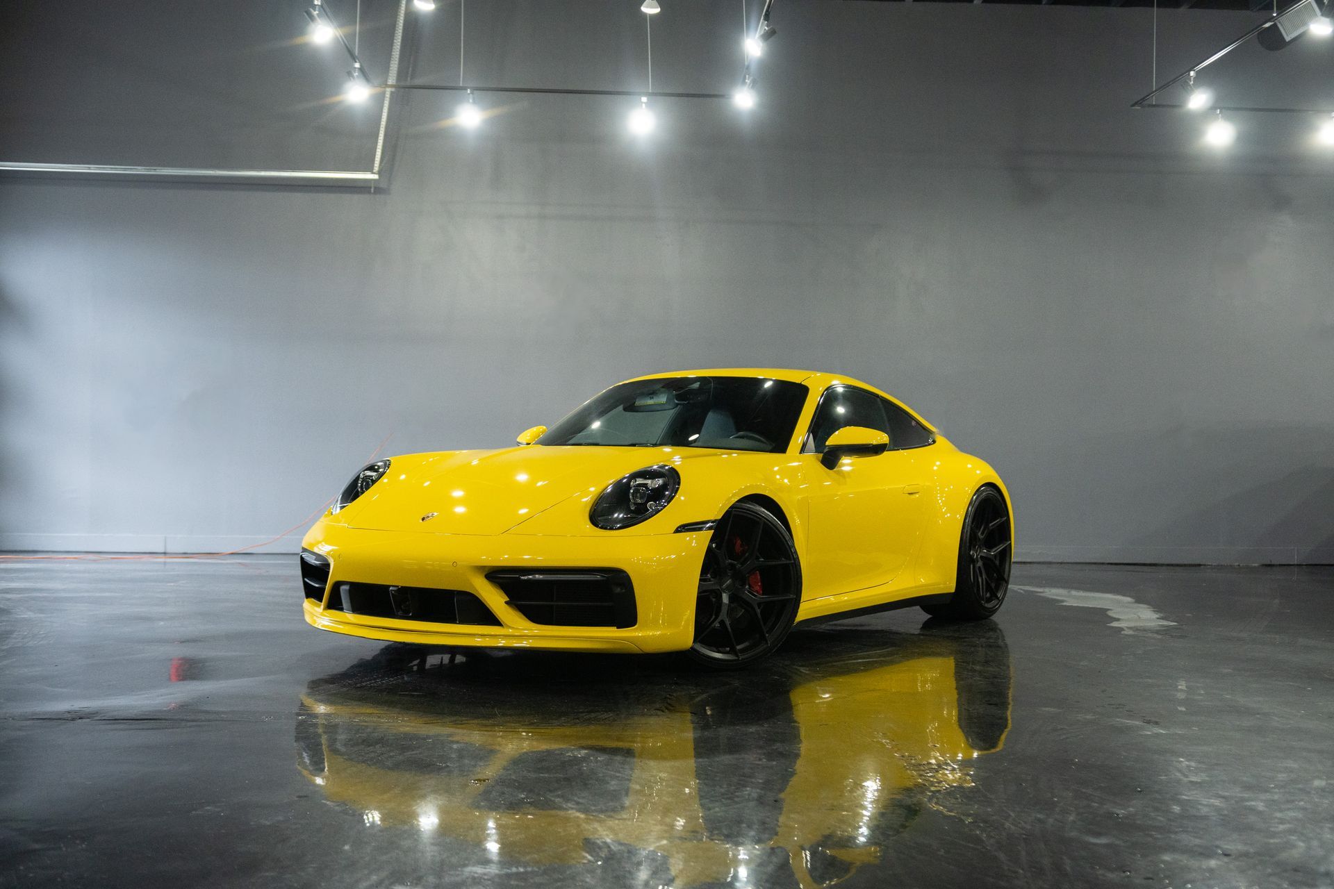 Yellow Porsche 911 sports car parked in a showroom, reflecting on the wet floor under bright lights.