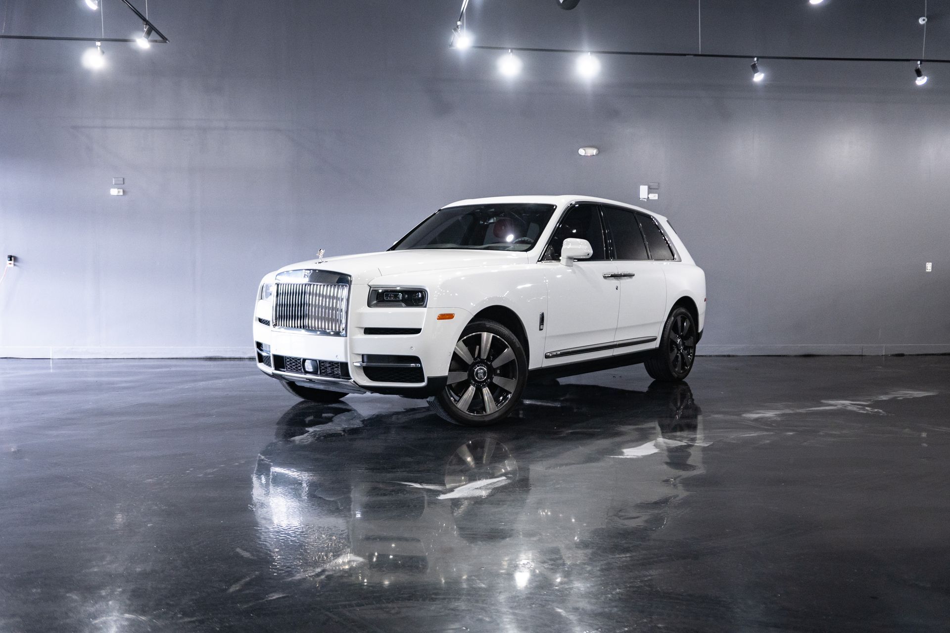 White Rolls Royce Cullinan SUV parked on a shiny, reflective floor in a studio setting.