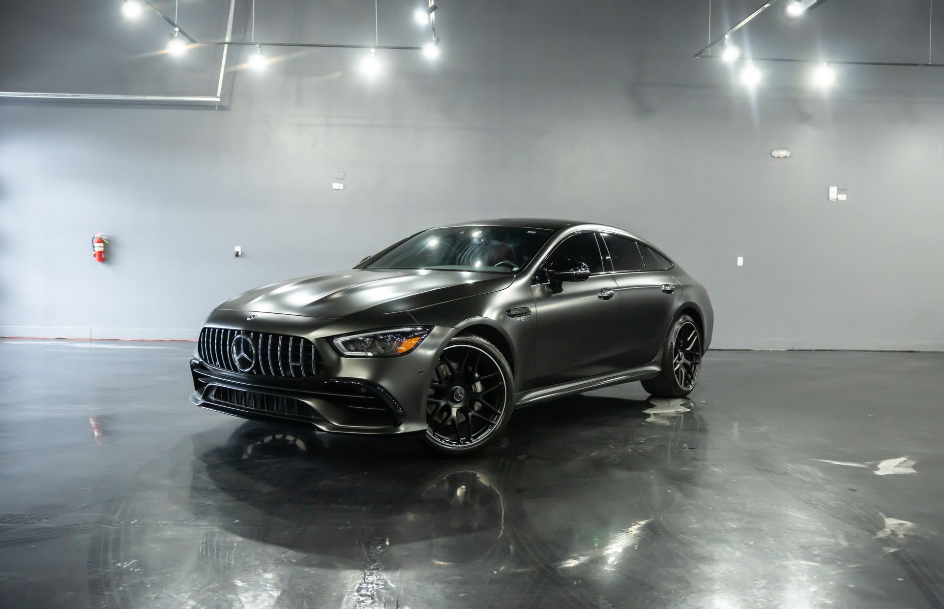 Gray Mercedes-AMG GT 4-door coupe in a spacious, glossy-floored showroom under bright lights.