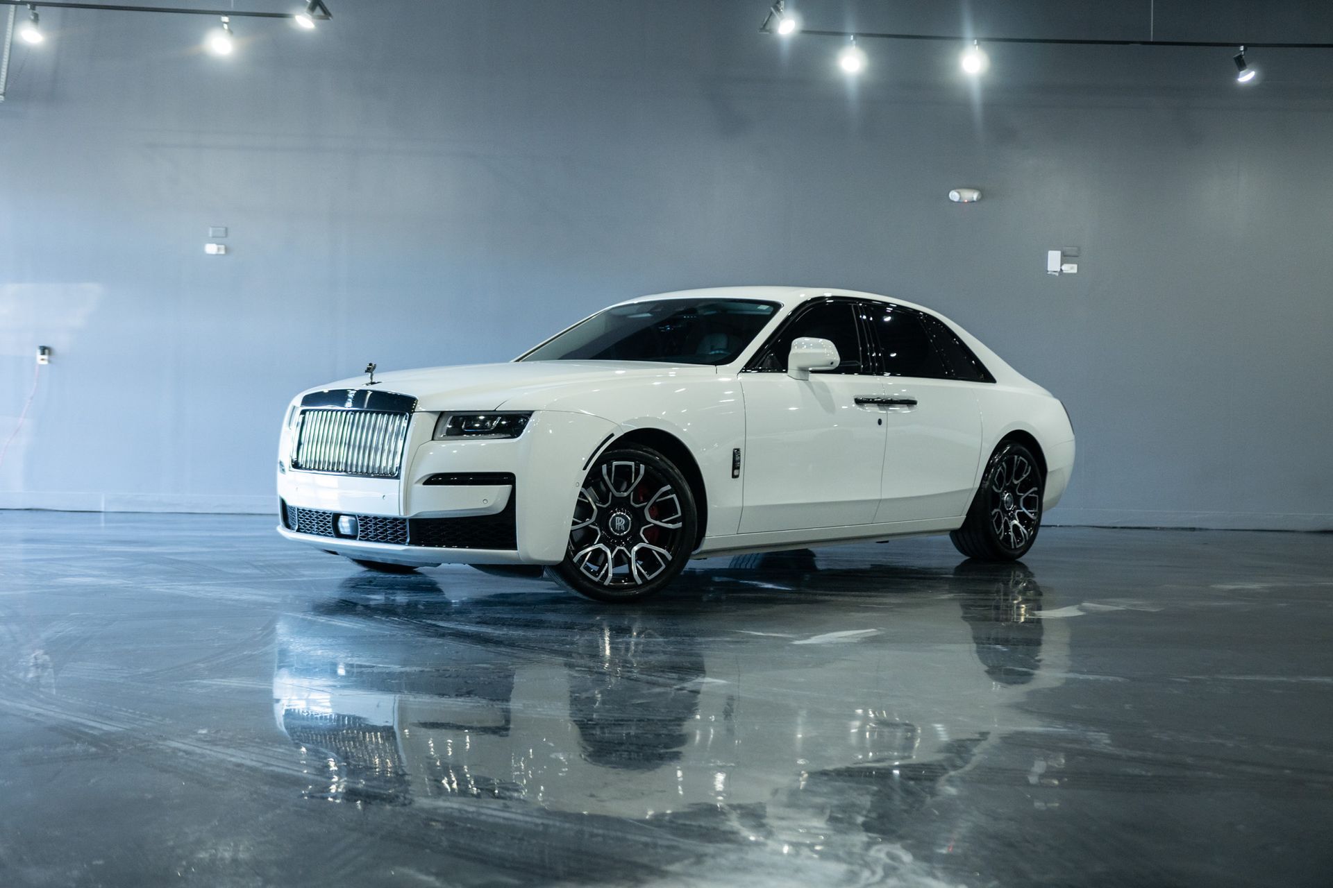 White Rolls-Royce sedan parked in a showroom with a shiny floor, reflected in the gloss.