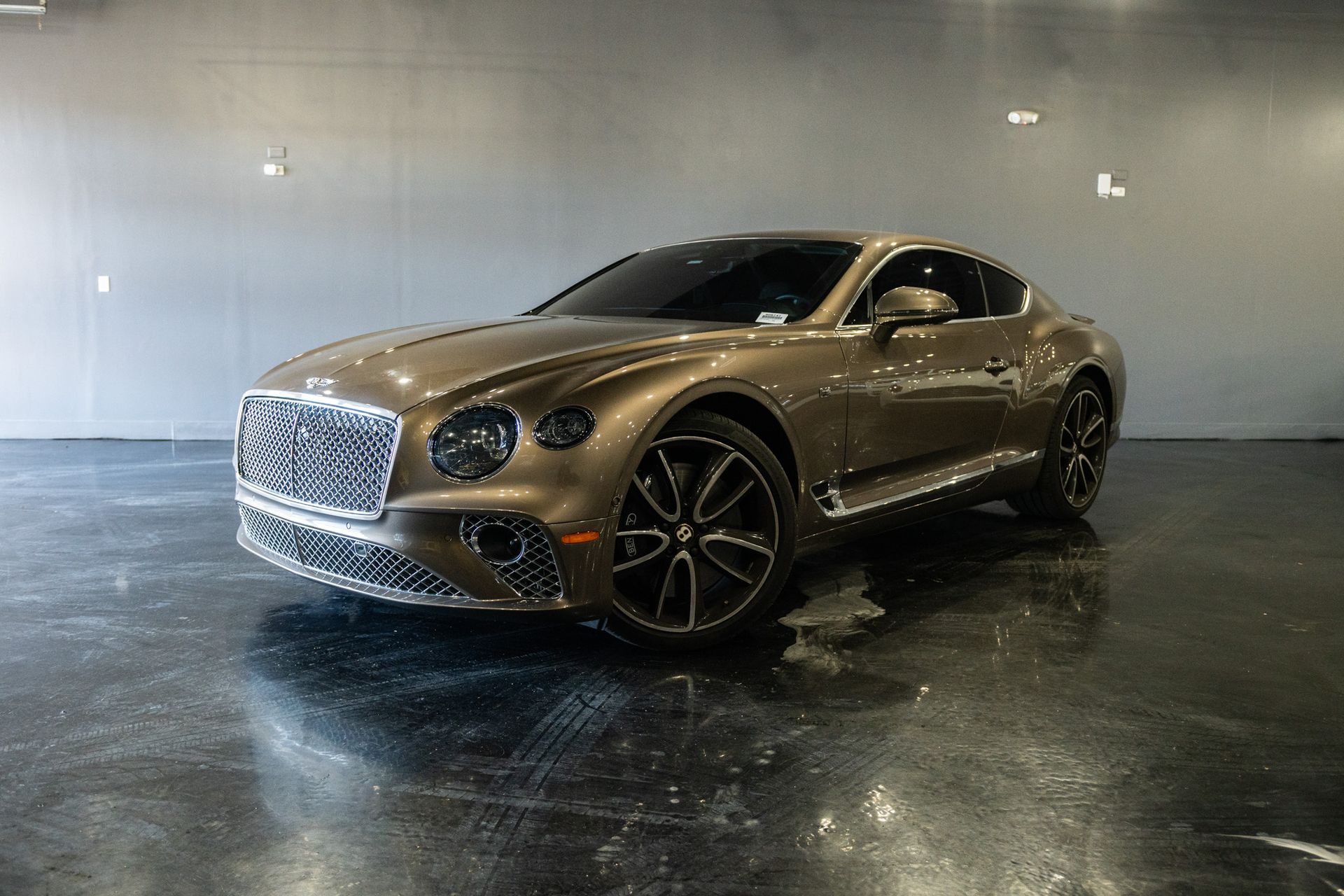 A brown Bentley coupe parked on a glossy surface. The car has a chrome grille and black wheels.