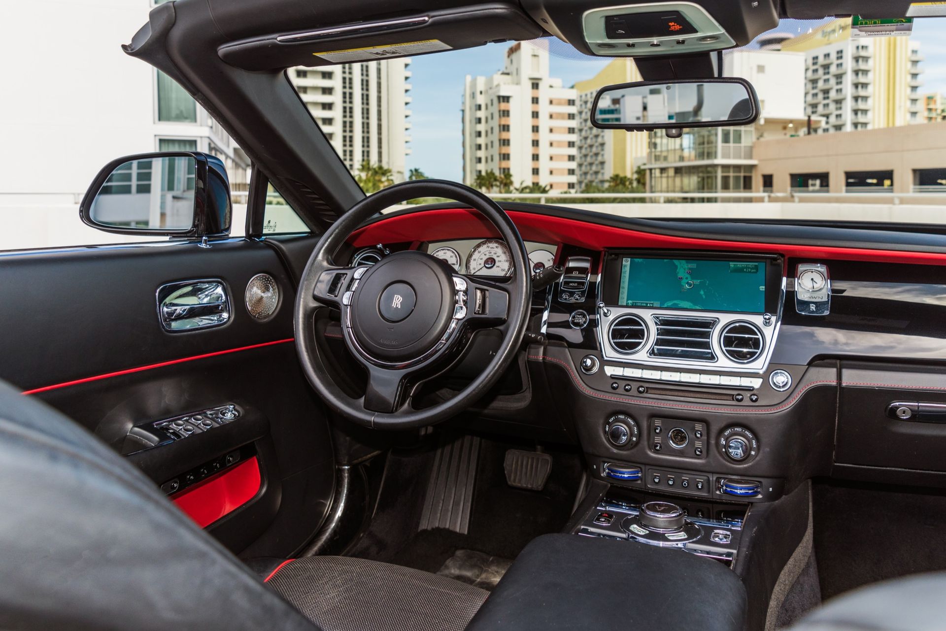 Interior of a black Rolls-Royce convertible with red trim, showing the dashboard, steering wheel, and navigation screen.