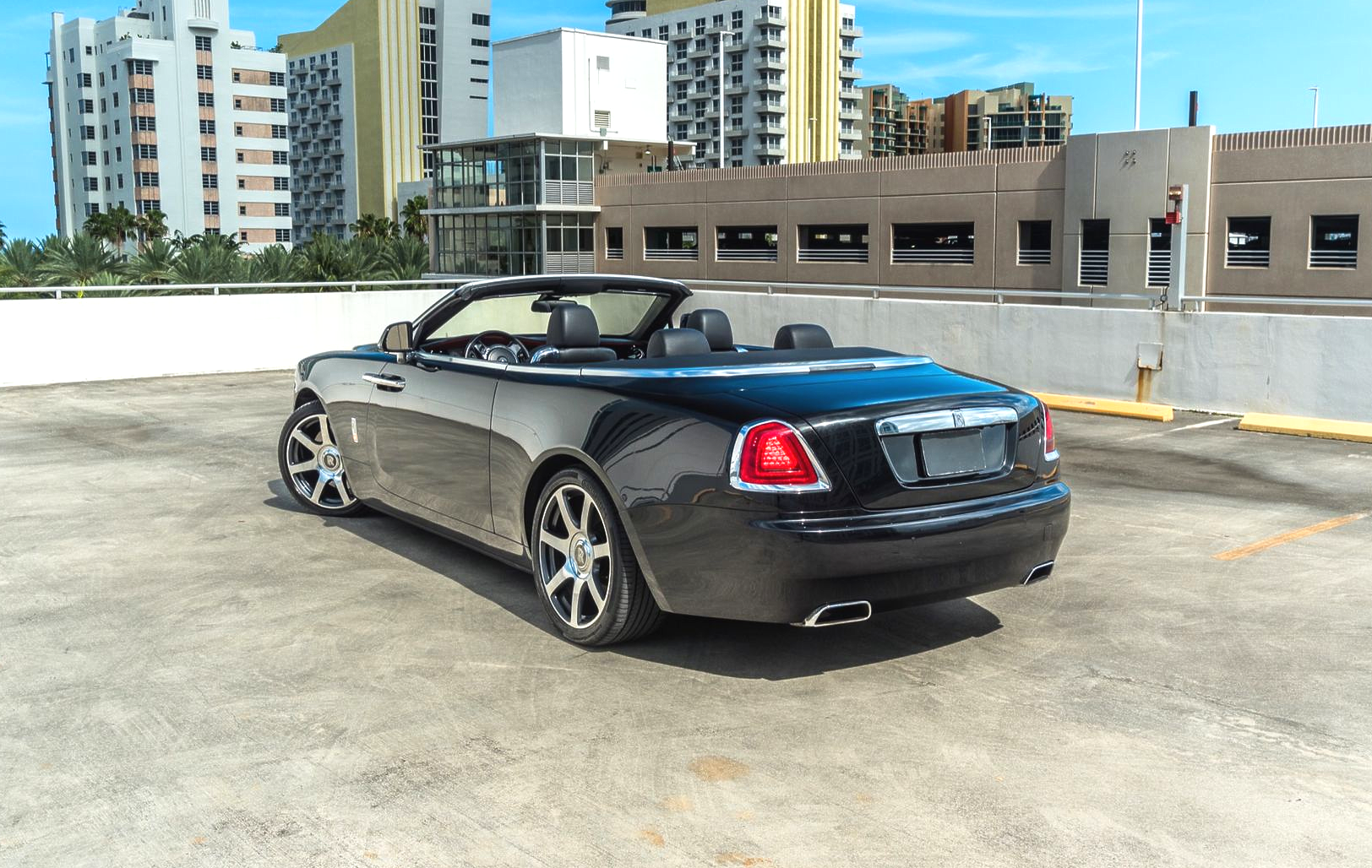 Black Rolls-Royce convertible parked on a rooftop parking lot with city buildings in the background.