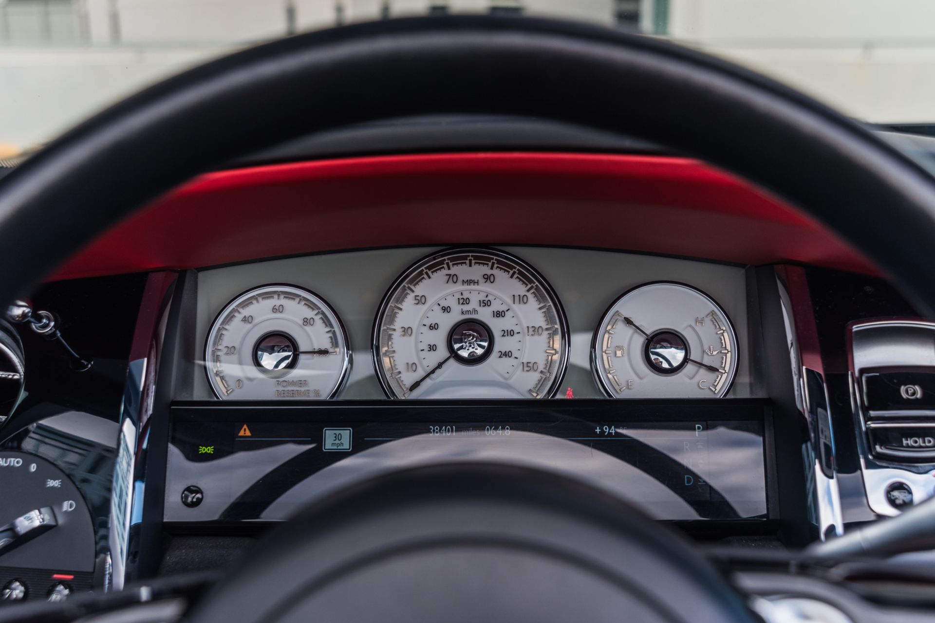 Dashboard of a luxury car with white gauges, red accents, and a black steering wheel.