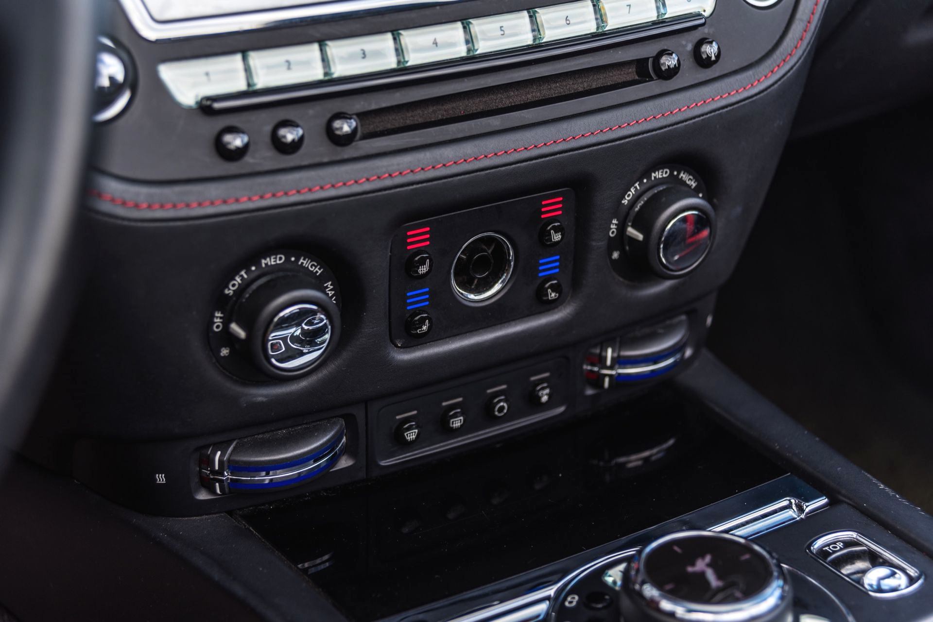 Black car dashboard with climate controls, silver accents, and red stitching.