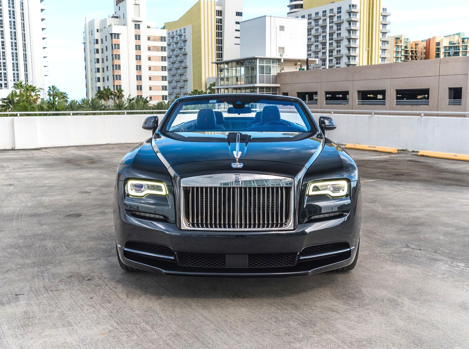 Black Rolls-Royce convertible parked on a rooftop, with city buildings in the background.