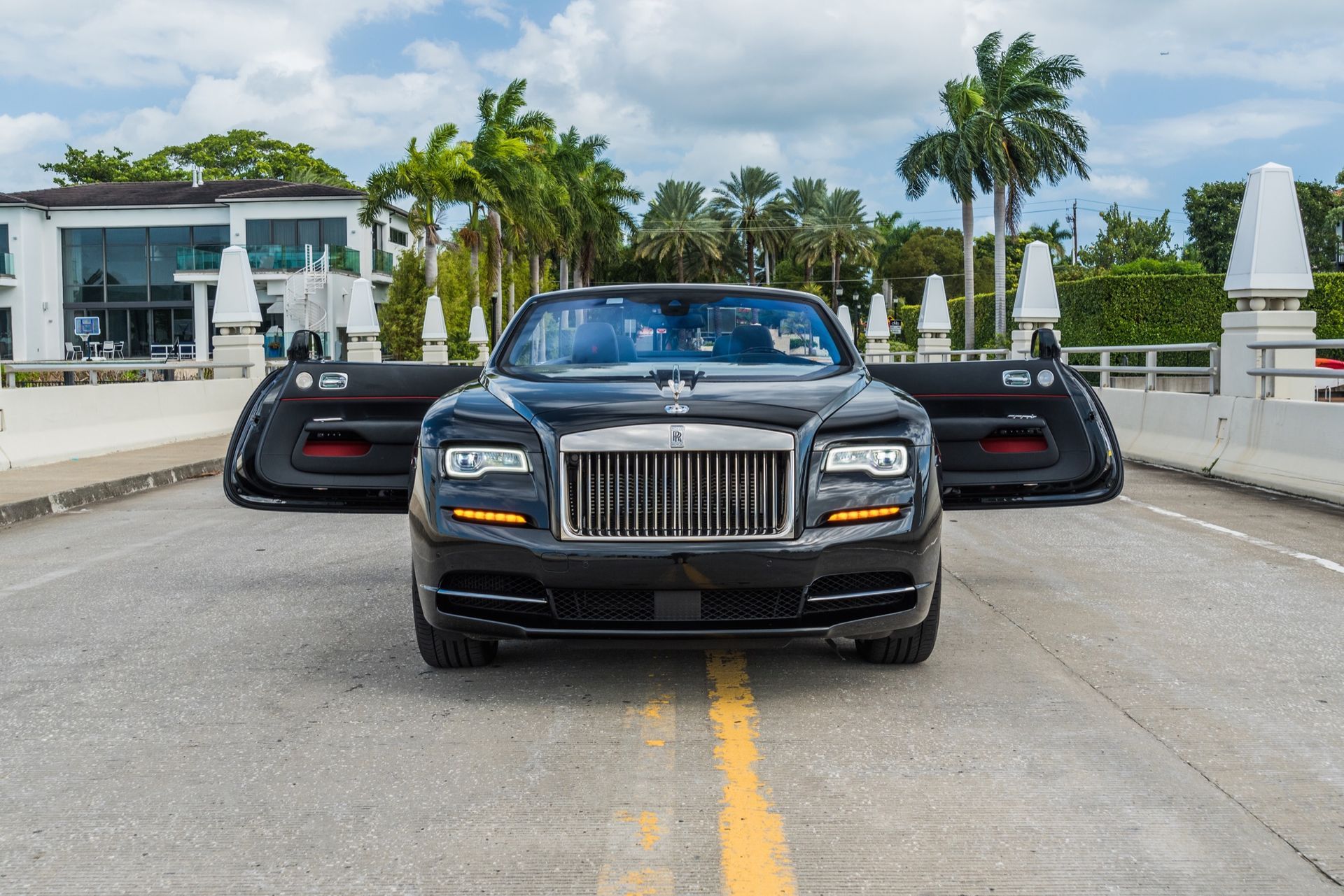 Black Rolls-Royce with doors open on a bridge, palms trees in the background.
