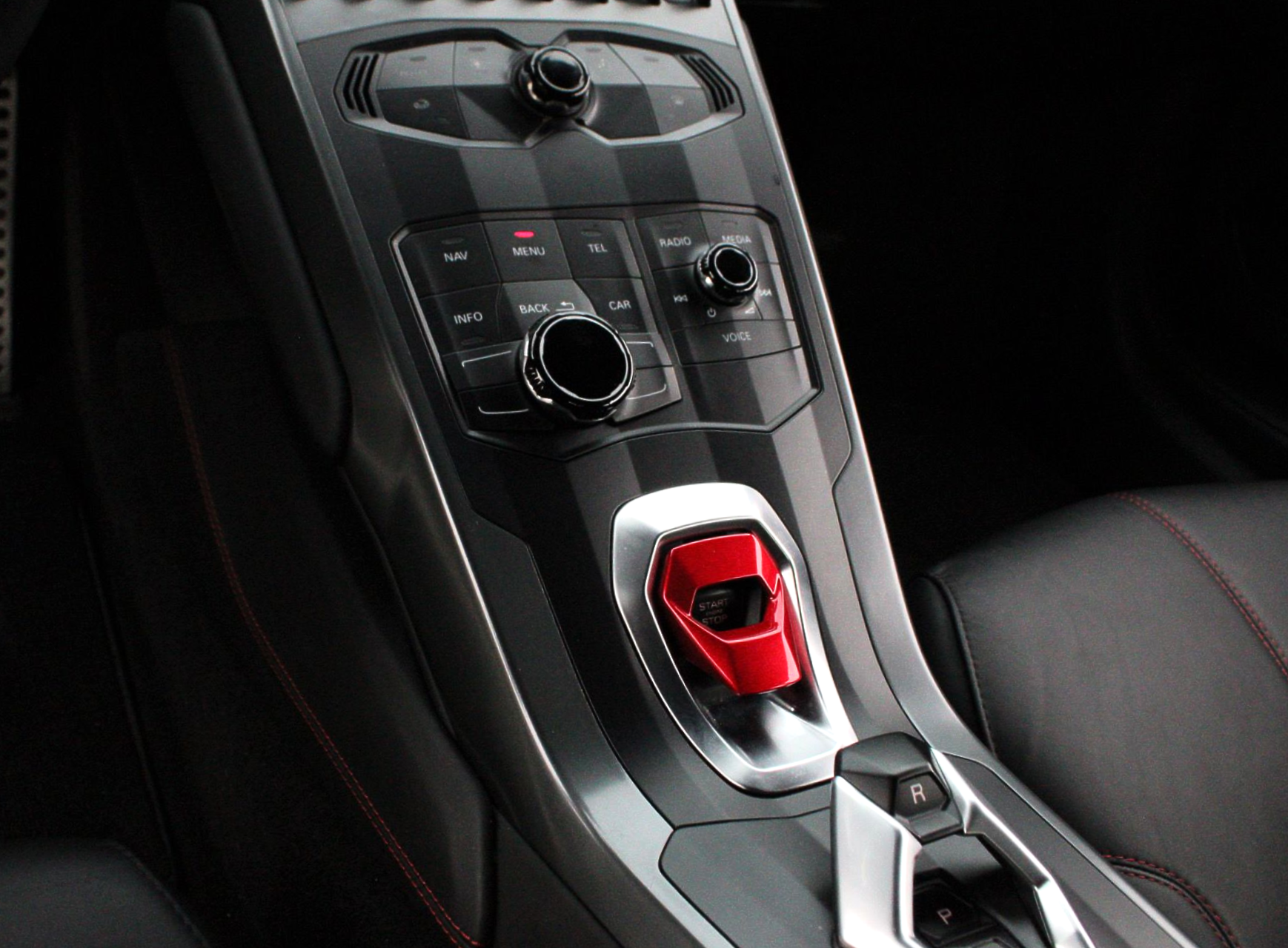 Interior of a Lamborghini, center console with red start button and climate controls.