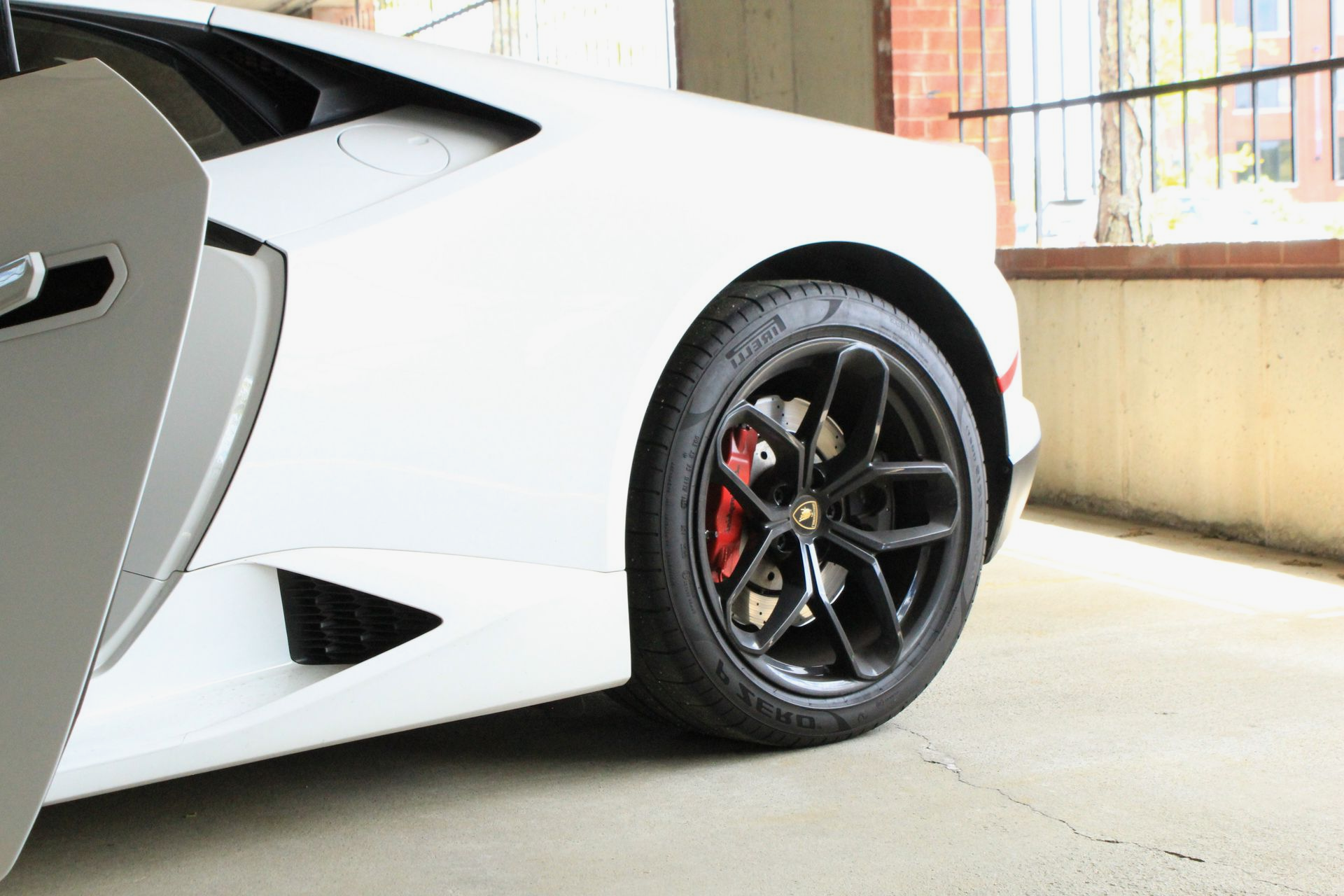 White Lamborghini with the door open, black wheels, red brake calipers.