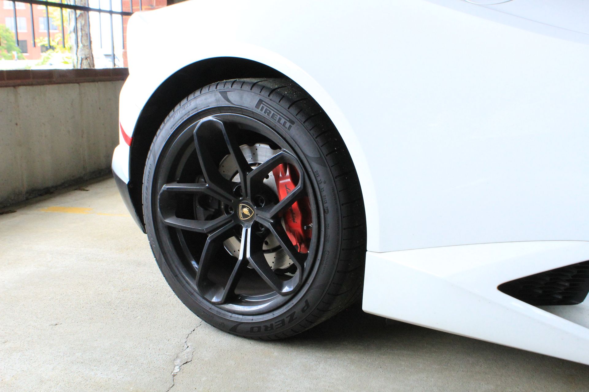 White Lamborghini sports car's black wheel with red brake caliper.