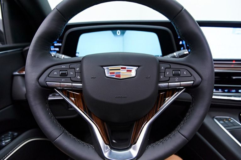 Cadillac steering wheel with wood grain accents, controls, and dashboard in the background.