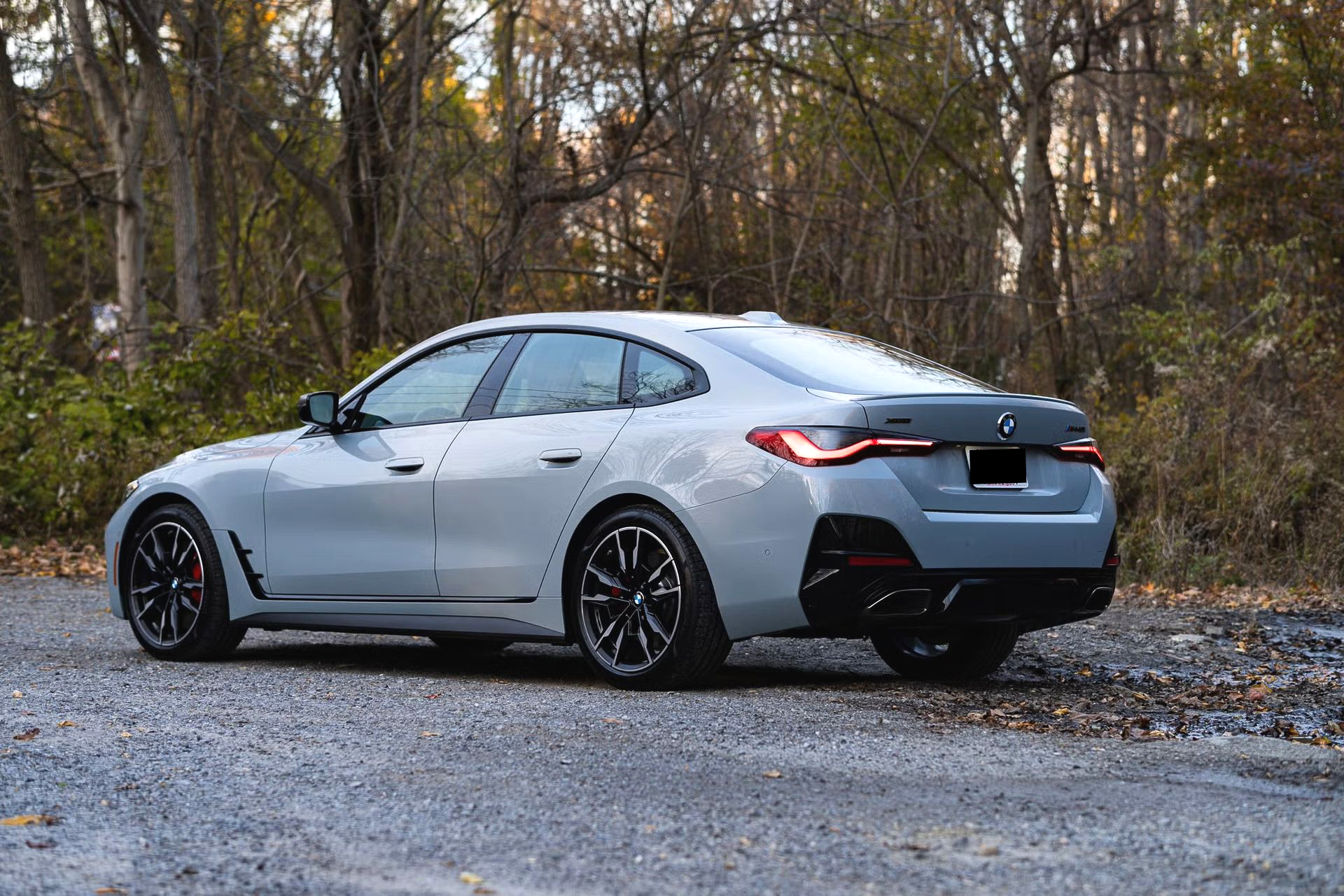 Gray BMW sedan parked on gravel road with trees in background.