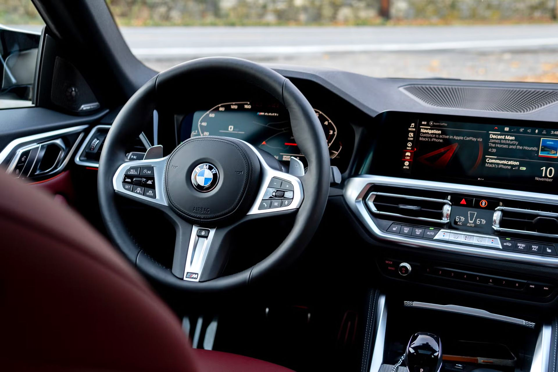 Interior of a BMW car with a black steering wheel, digital display, and red leather seats.