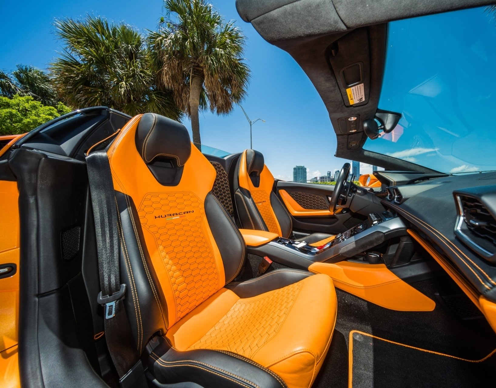 Orange and black convertible car interior with a blue sky and palm trees in the background.