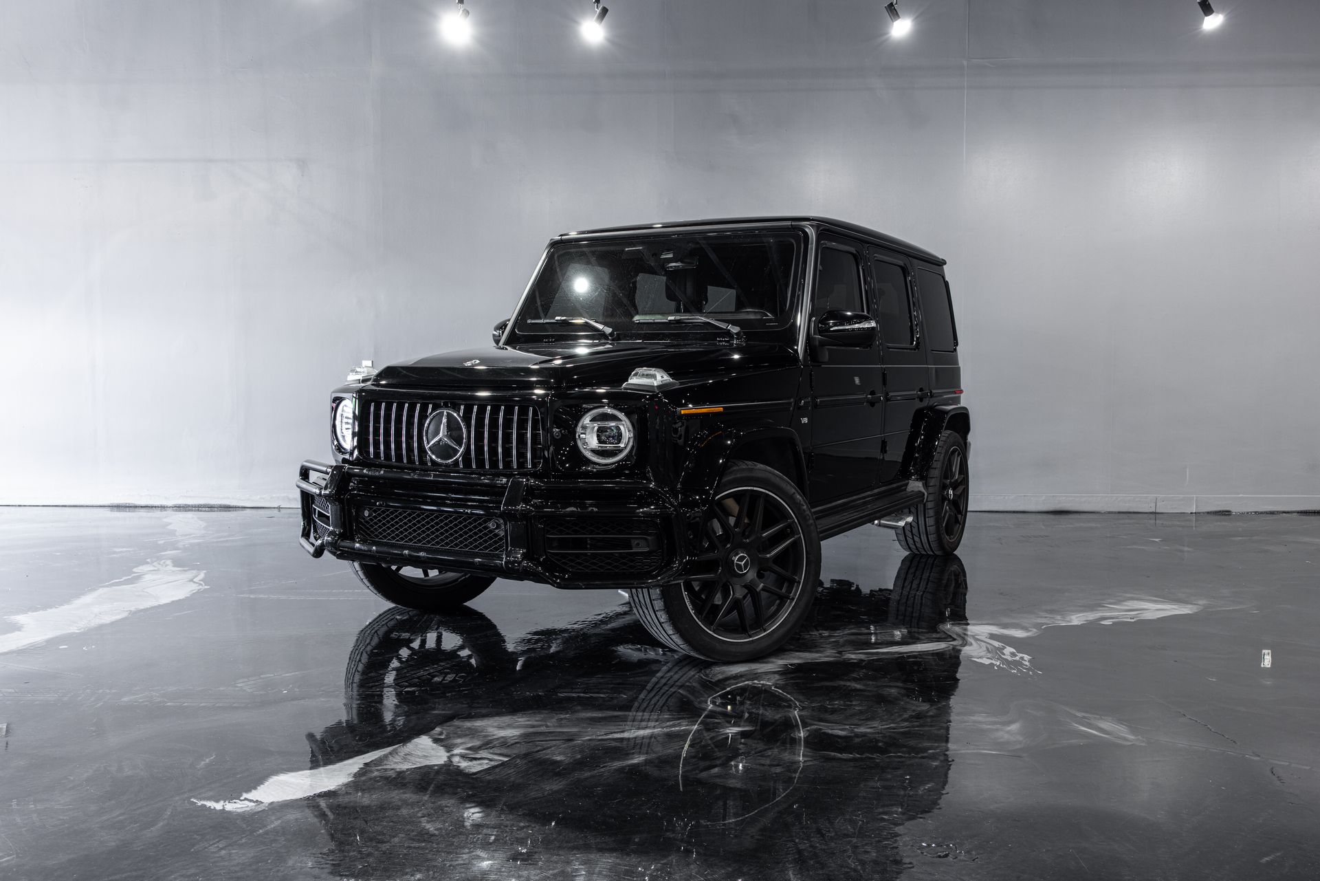 Black Mercedes-Benz G-Class SUV parked on a glossy, wet surface in a studio setting.