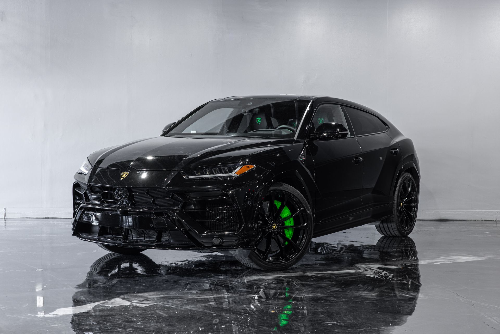 Black Lamborghini Urus SUV with bright green brake calipers, in a studio setting.