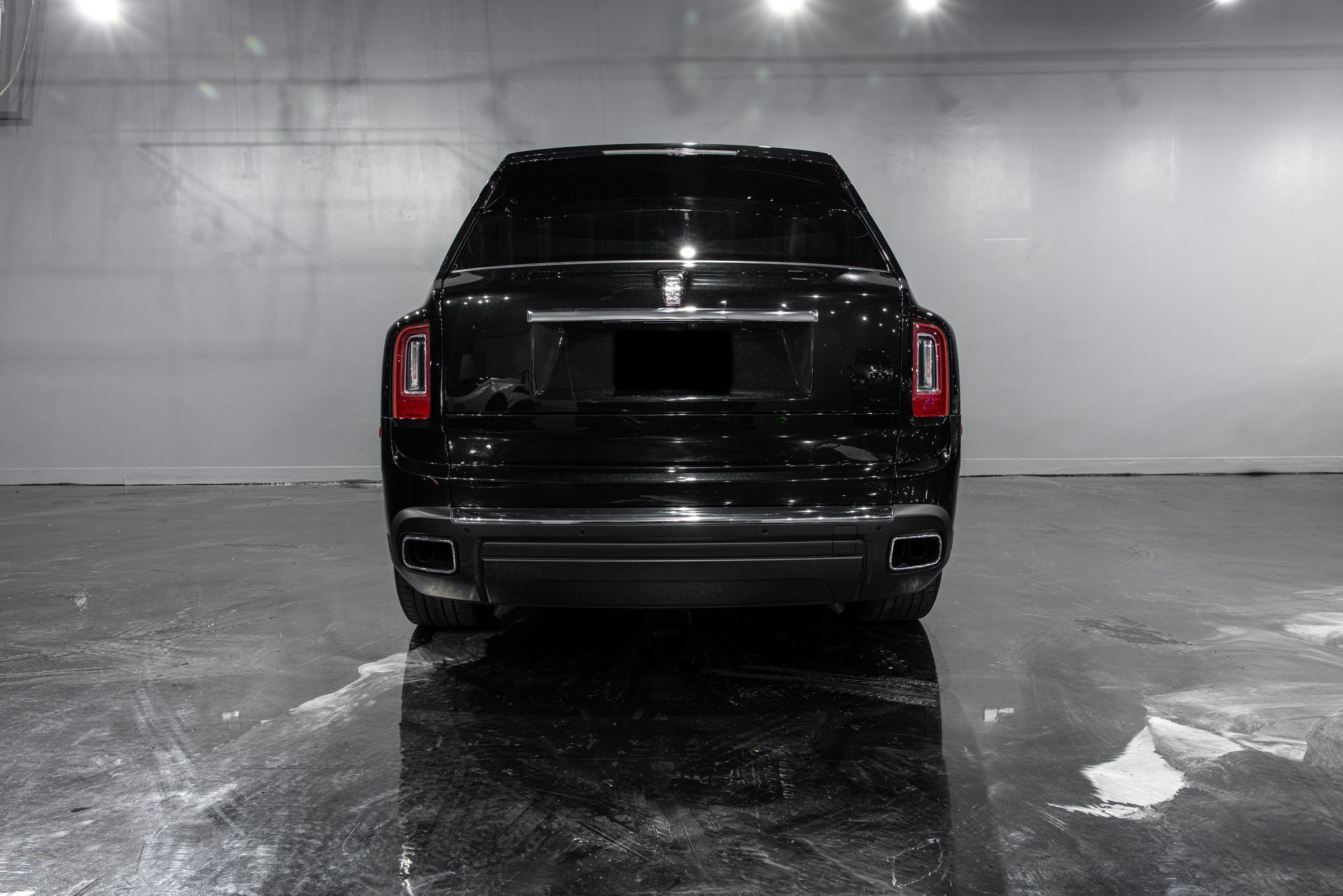 Black Rolls Royce SUV, rear view in a gray-walled garage, reflecting on the floor.