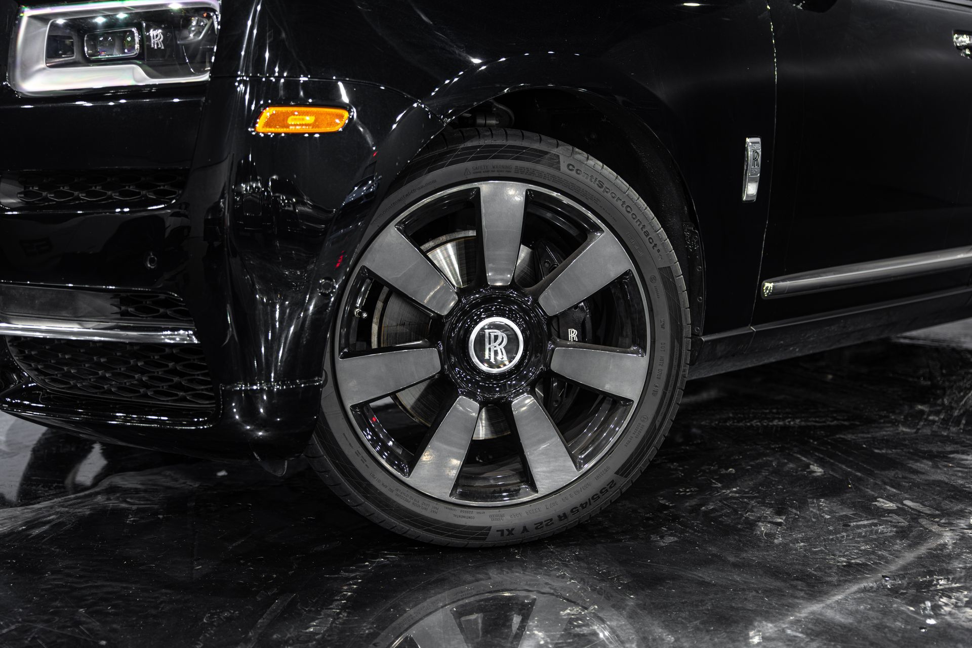 Black Rolls Royce front wheel, dark gray rim design, on shiny black surface.