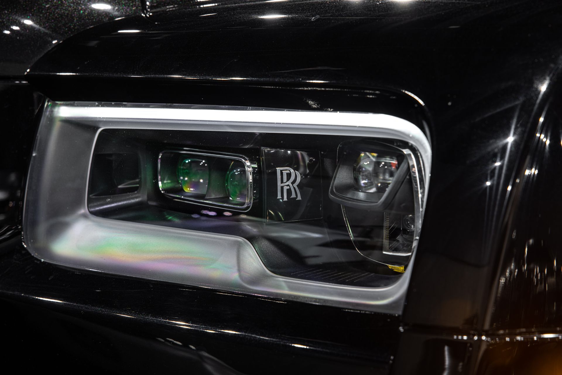 Close-up of a Rolls-Royce headlight; black car with the Rolls-Royce emblem visible.