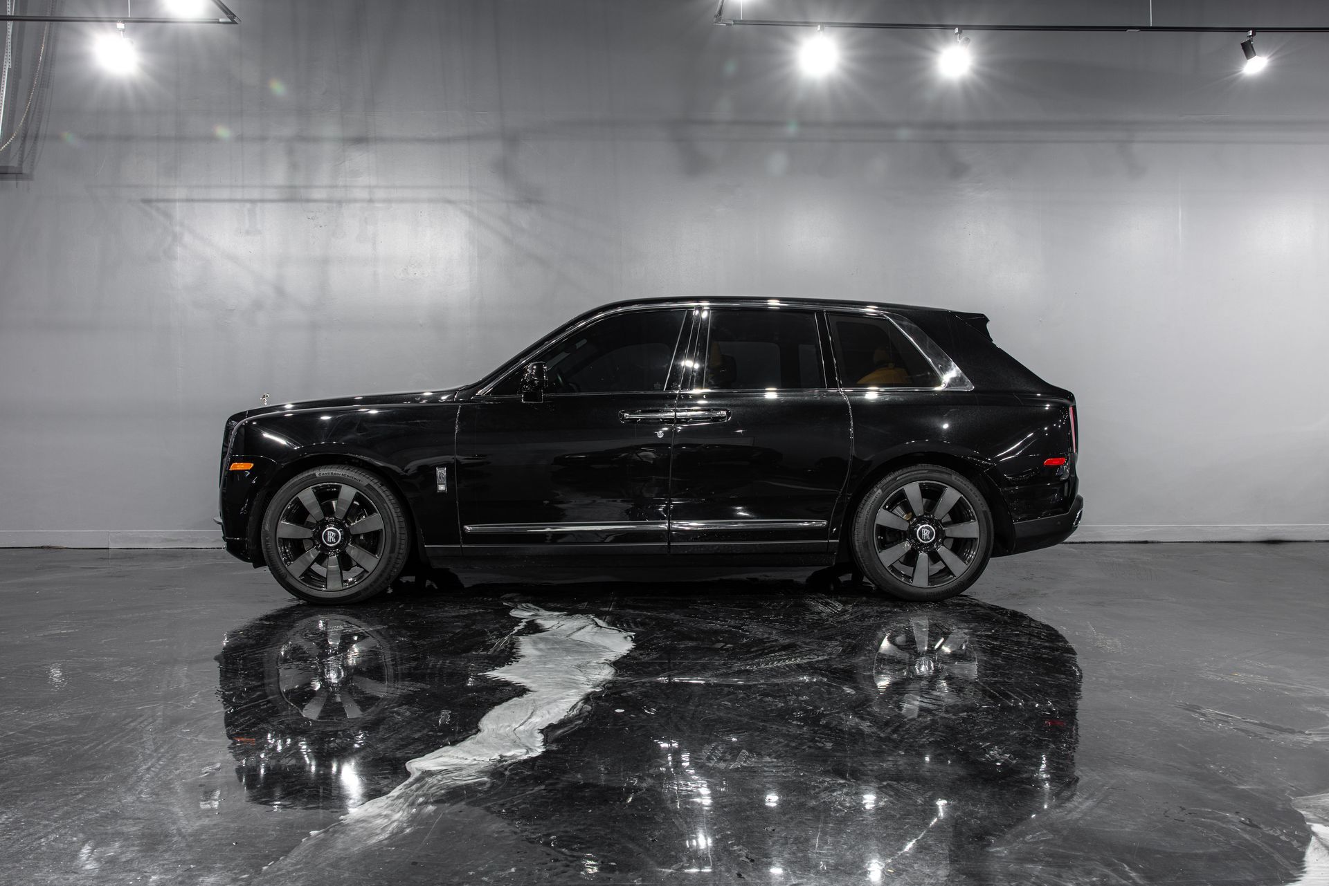 Black Rolls-Royce Cullinan SUV parked on a reflective floor in a studio.