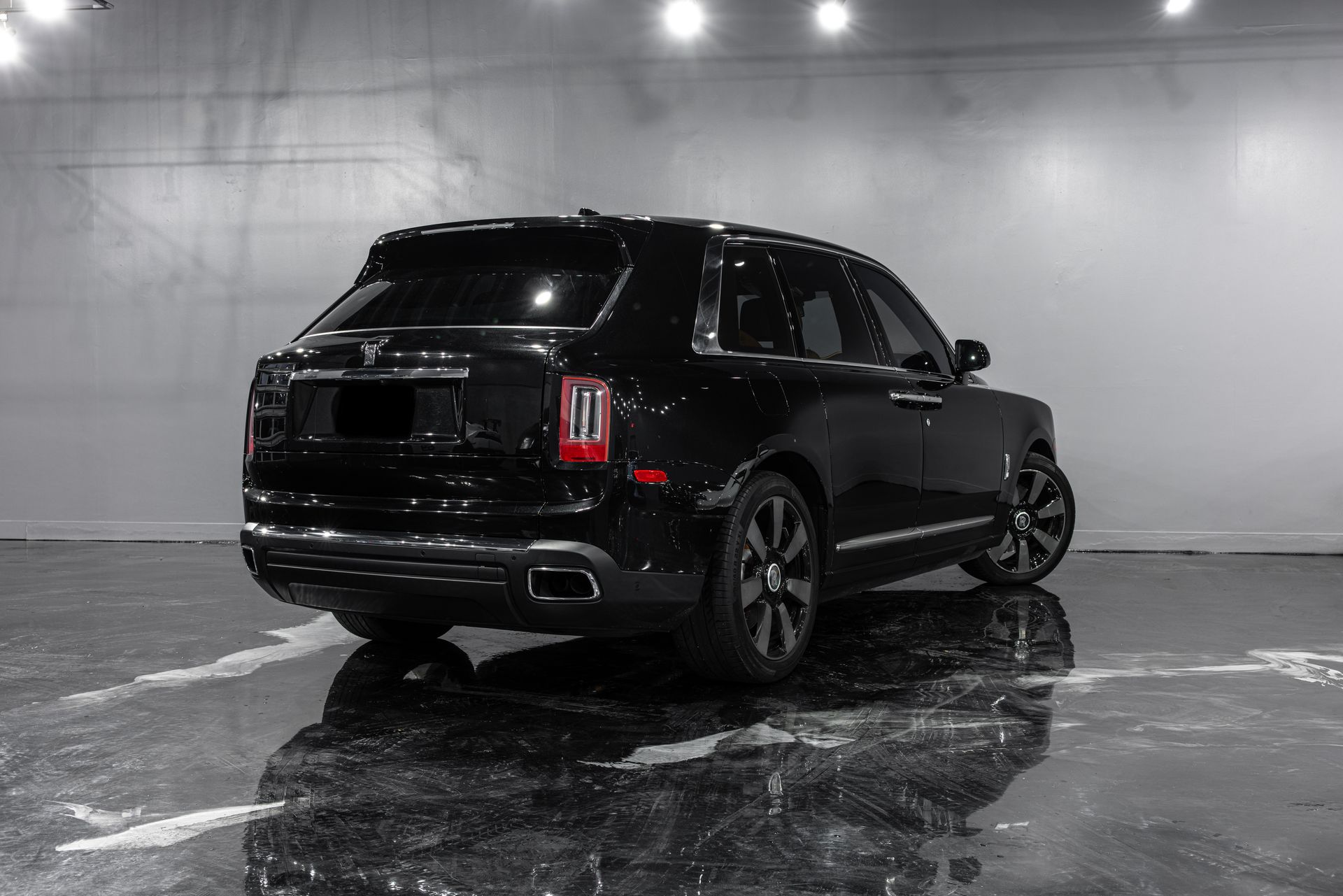 Black Rolls-Royce Cullinan SUV in a studio with a reflective floor and bright overhead lights.