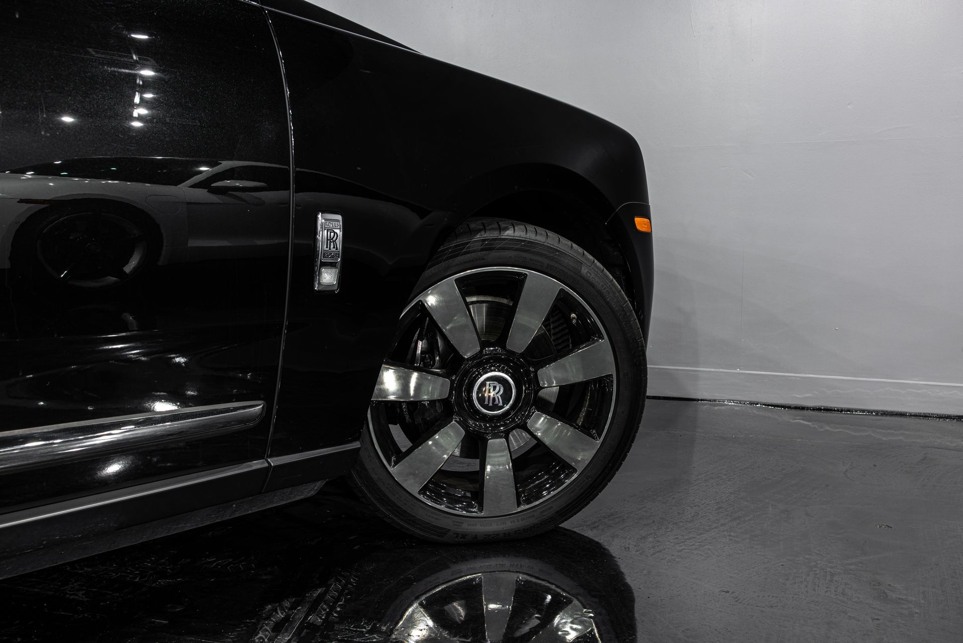 Black Rolls Royce car wheel and front panel in a showroom with reflections.