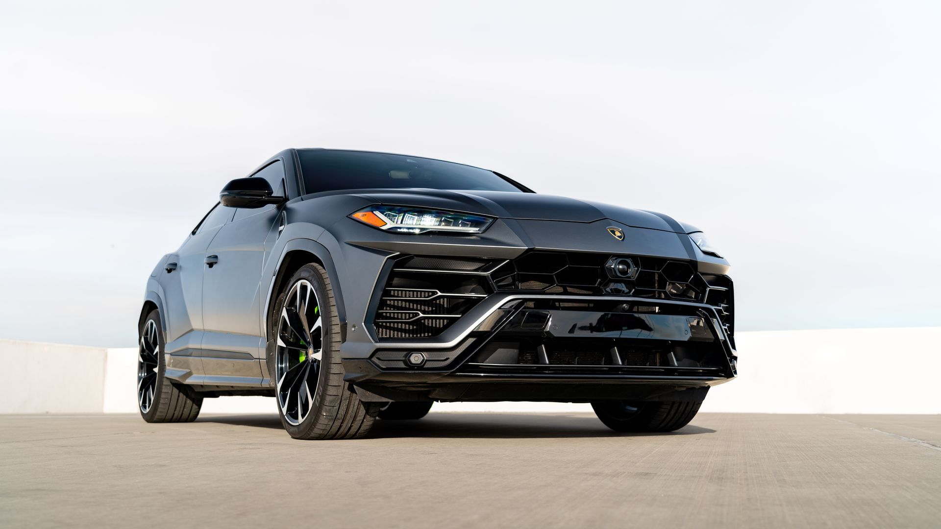 Gray Lamborghini Urus SUV on a concrete surface under a bright sky.