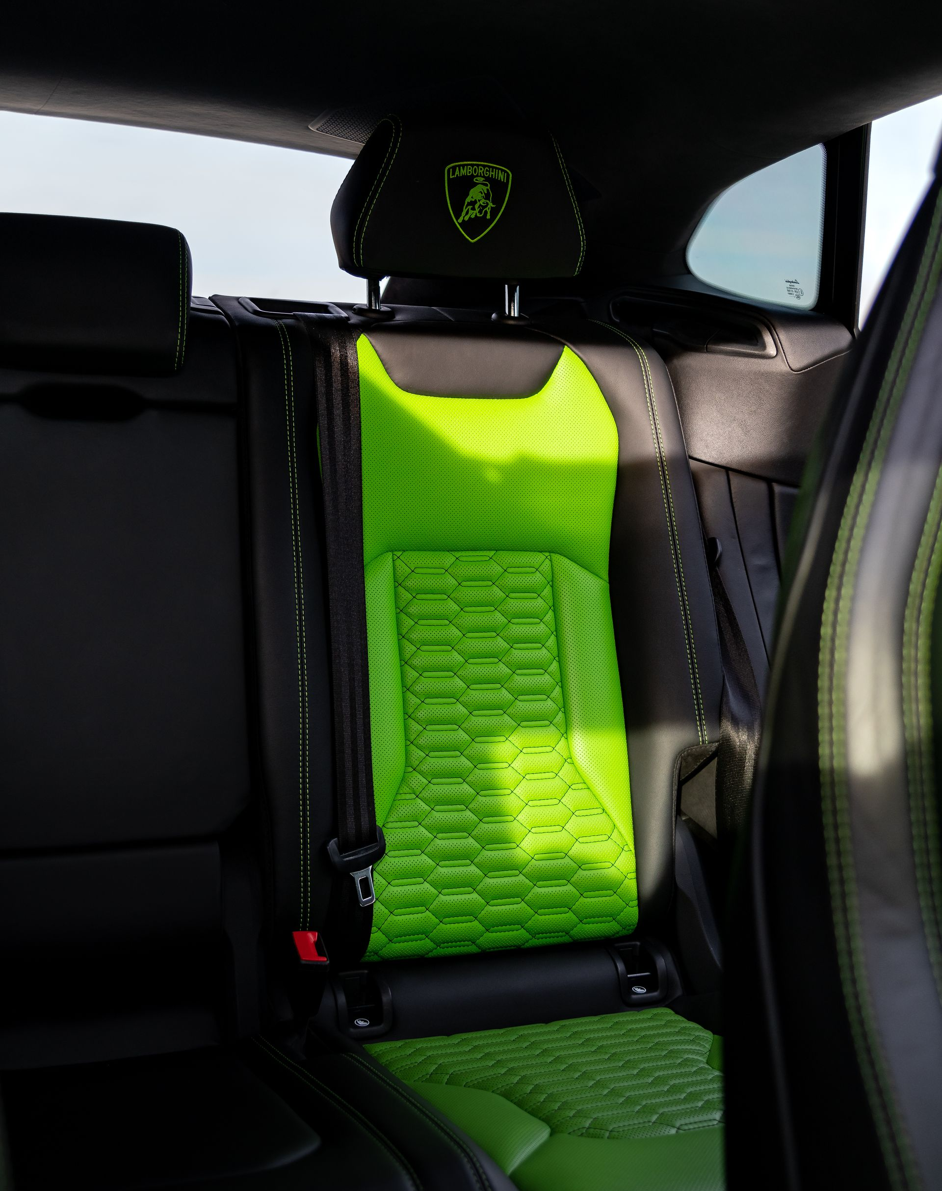 Rear seat interior of a Lamborghini with a neon green car seat installed; black and green stitching and a logo on headrest.