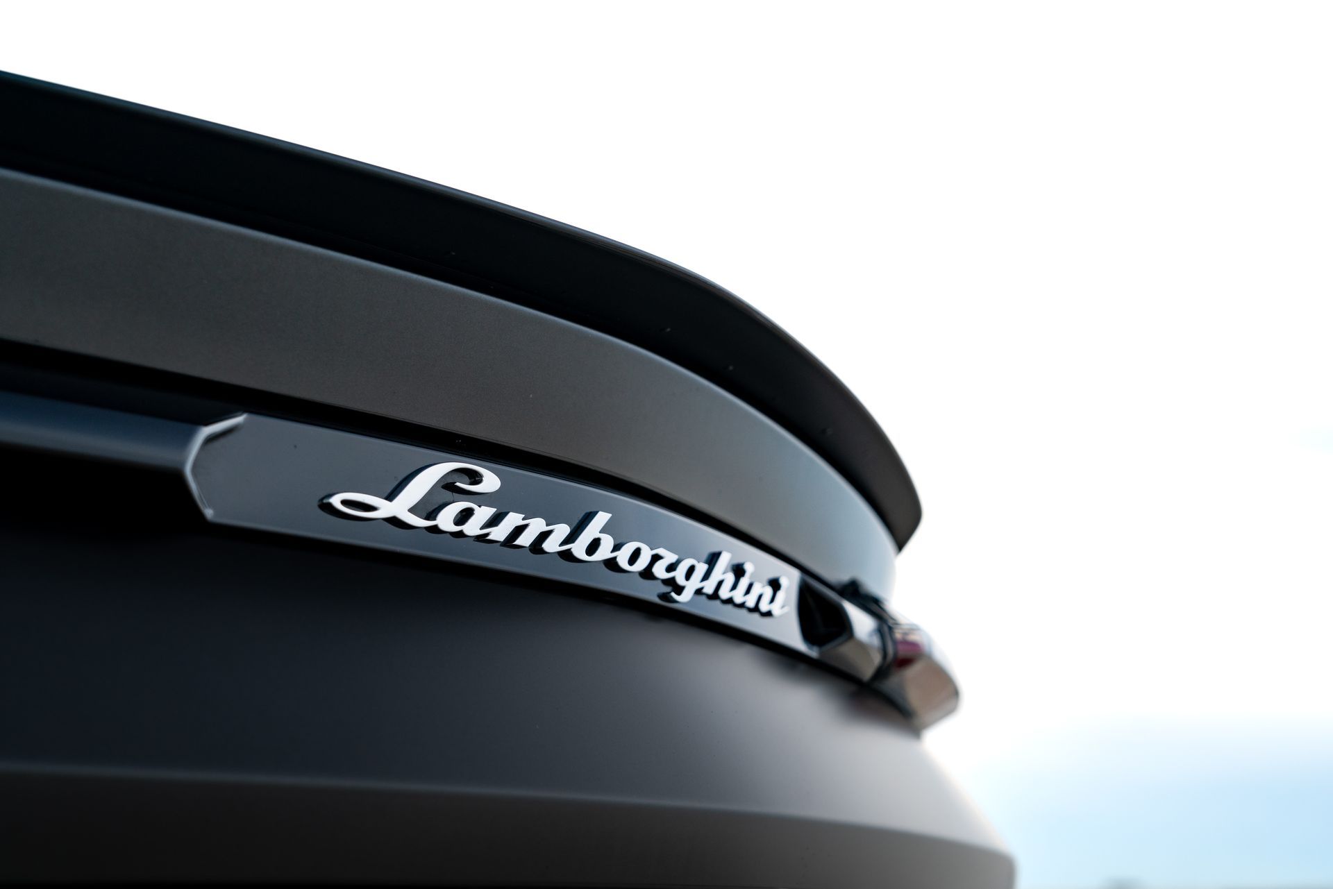 Lamborghini logo on a black car's rear, close-up against a bright sky.