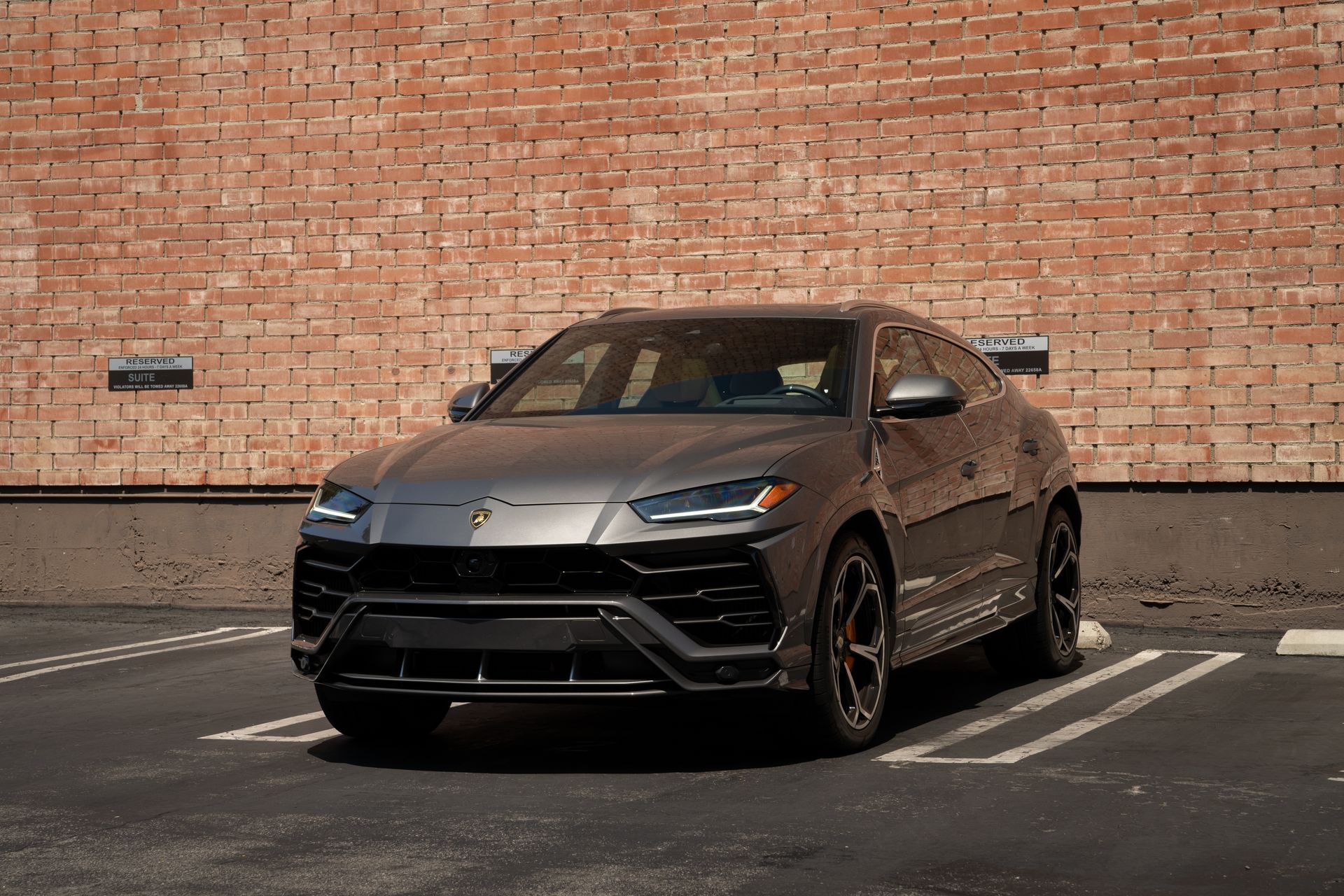 Gray Lamborghini SUV parked in a parking space in front of a brick wall.