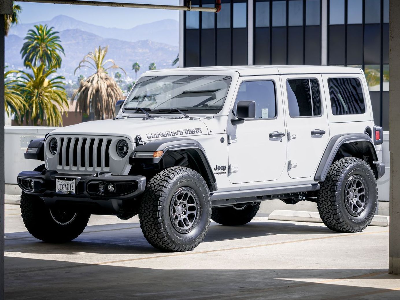 White Jeep Wrangler Rubicon parked in a city setting with palm trees in the background.
