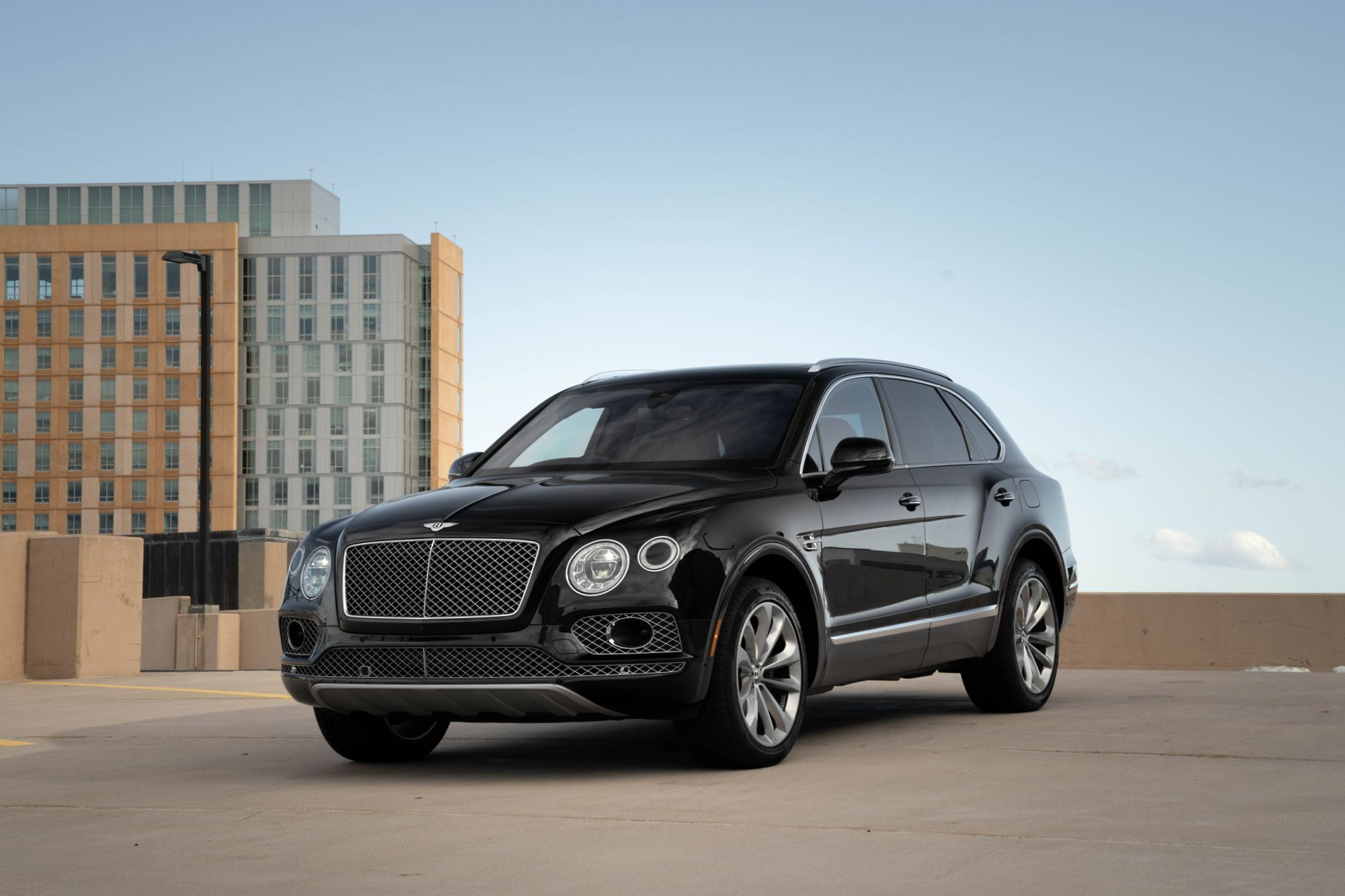 Black Bentley Bentayga SUV parked on a rooftop, with a city skyline in the background.