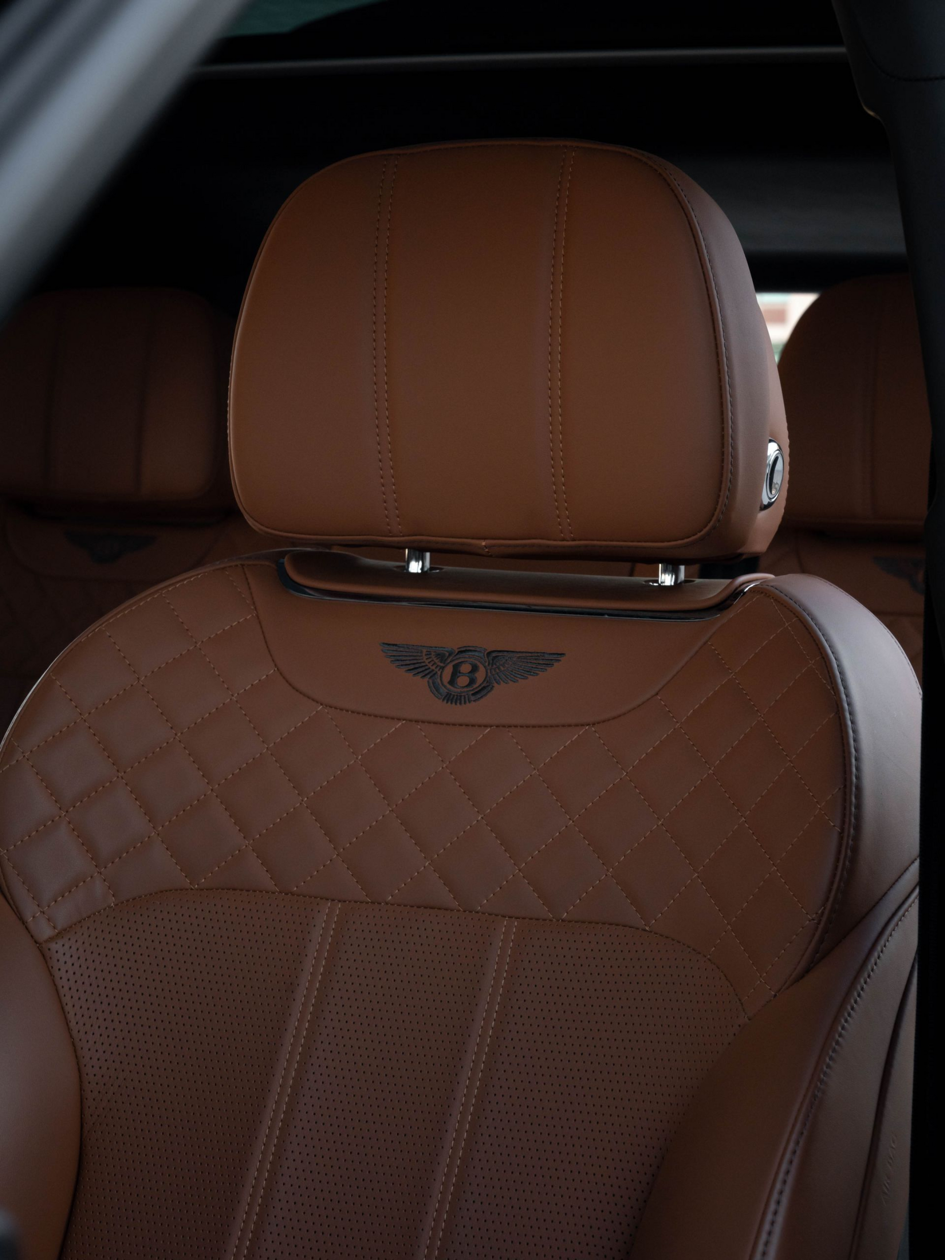 Brown leather Bentley car seat with quilted pattern, headrest with logo.