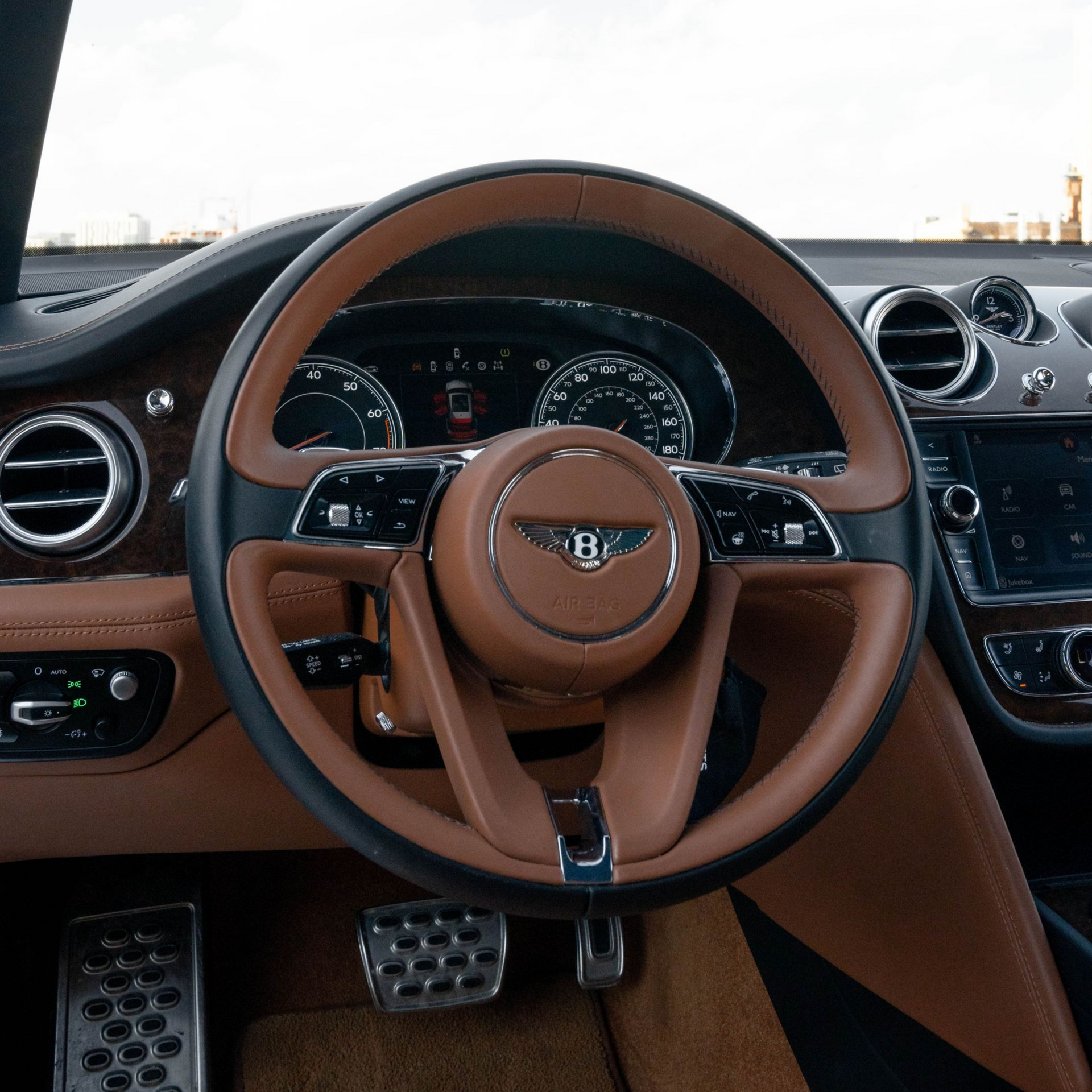 Brown leather Bentley steering wheel, dashboard, pedals, and surrounding interior.