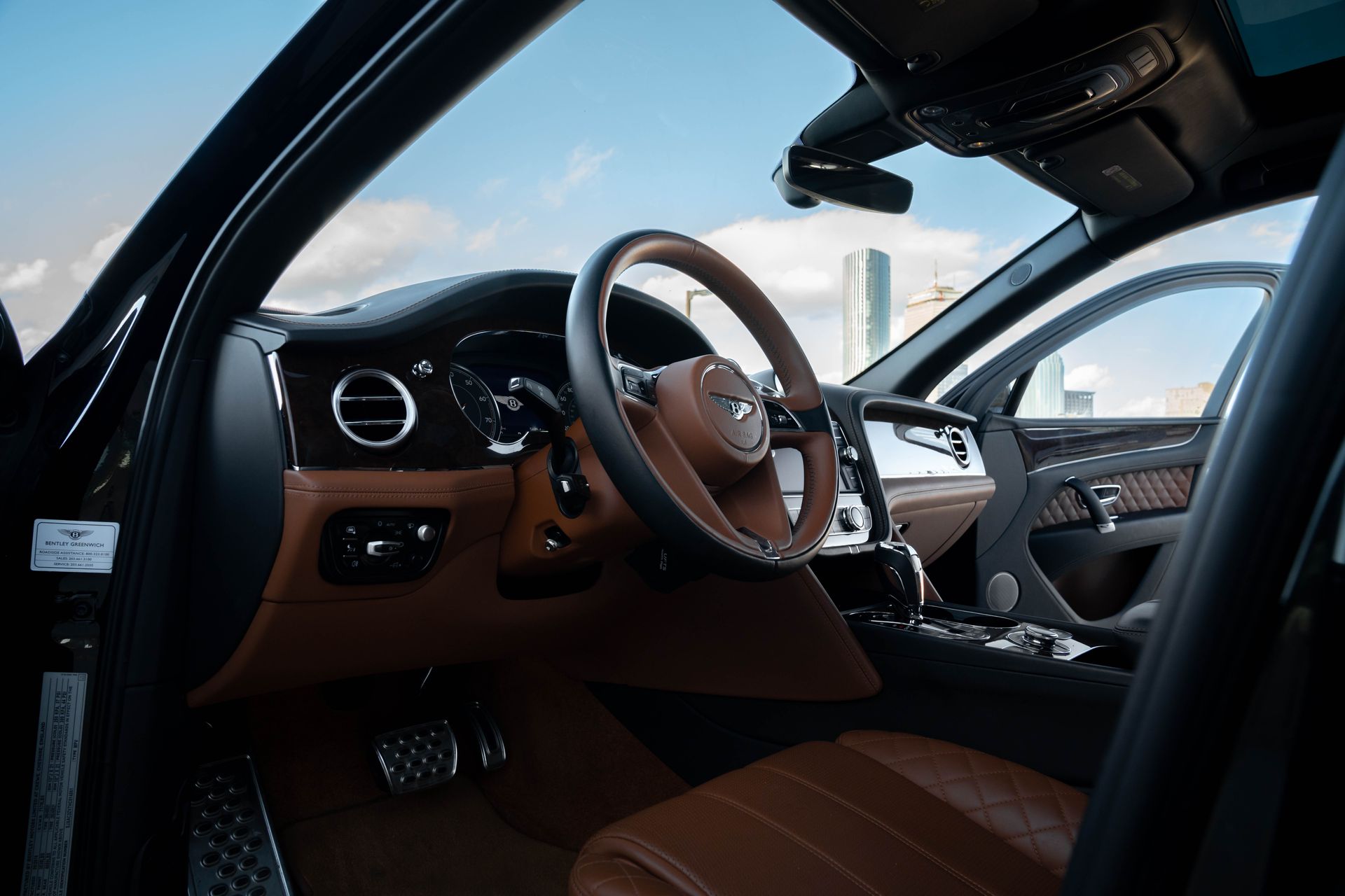 Interior view of a luxury car with brown leather seats and steering wheel, wood trim, and a blue sky visible.