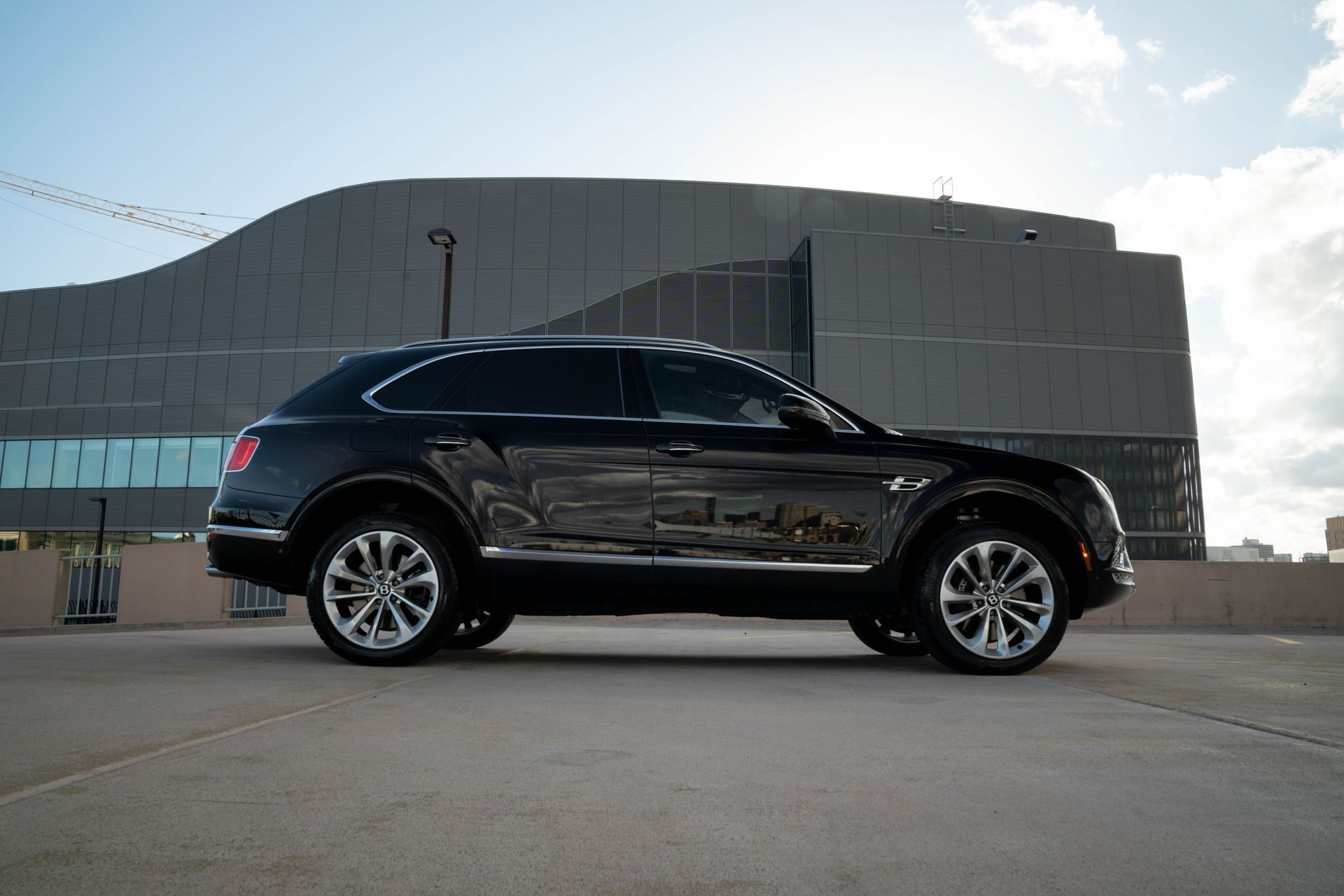 Black Bentley SUV parked on a rooftop, with a modern building in the background. Sunny day.