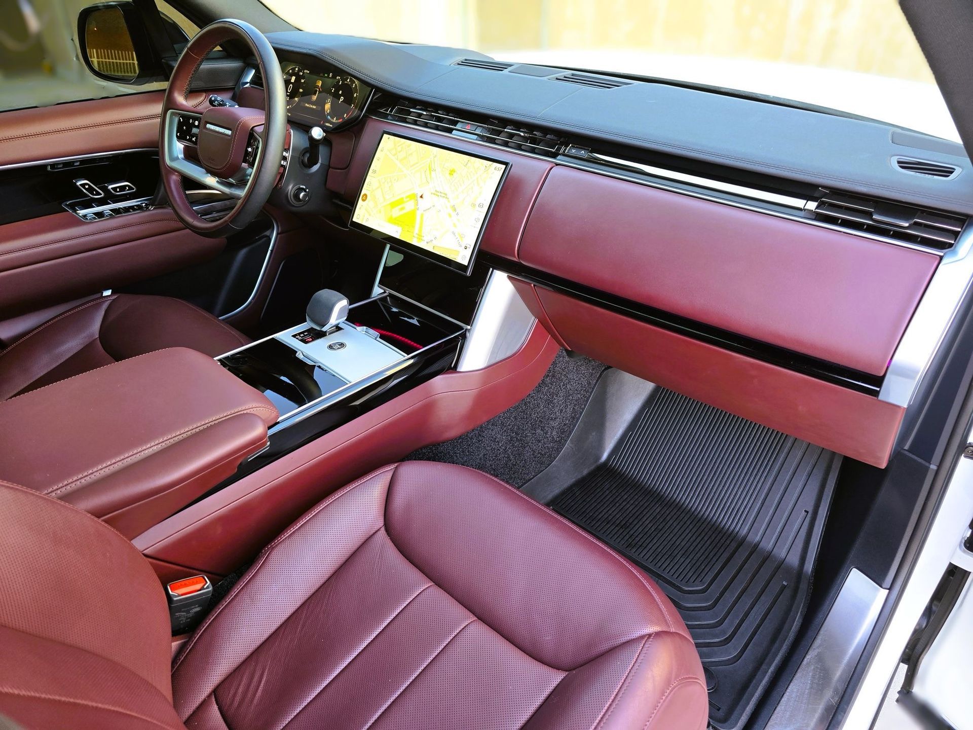 Burgundy leather interior of a luxury SUV, dashboard with infotainment screen, black floor mats.